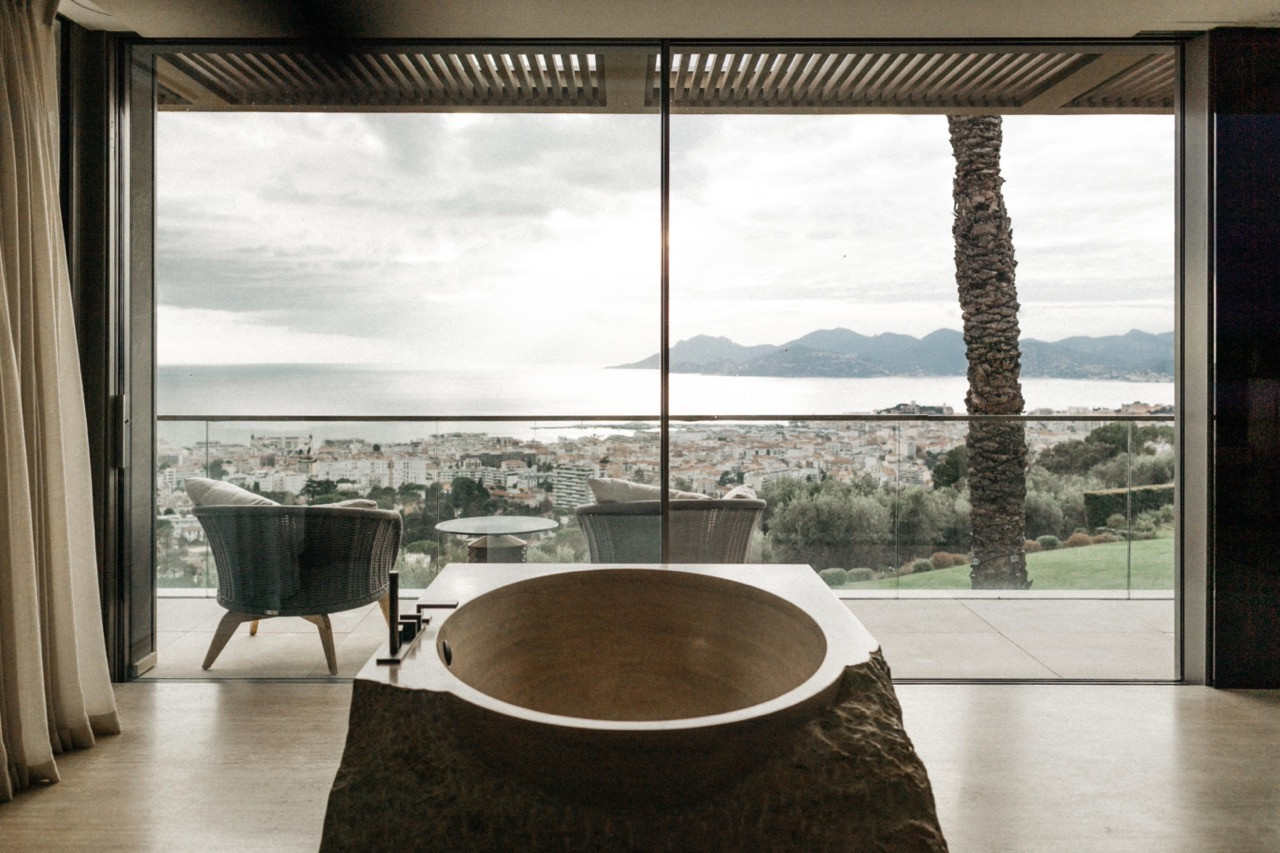 The travertine bathtub positioned before floor-to-ceiling glazing with views over Cannes and the Lérins Islands