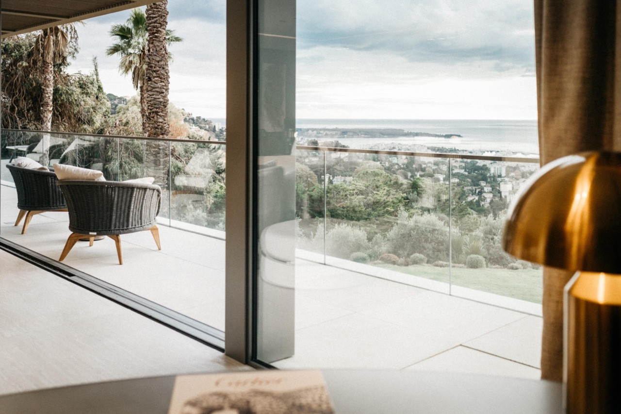 The terrace off the principal bedroom suite with wicker armchairs, glass balustrade and panoramic views over Cannes to the sea