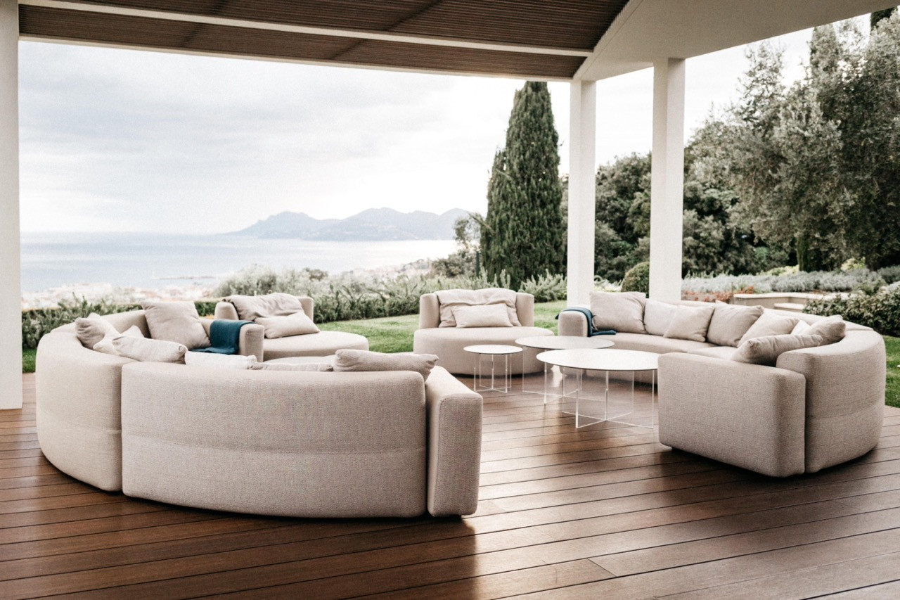 The covered outdoor terrace with two curved cream sectional sofas on a teak deck, with views over the Mediterranean and the Lérins Islands