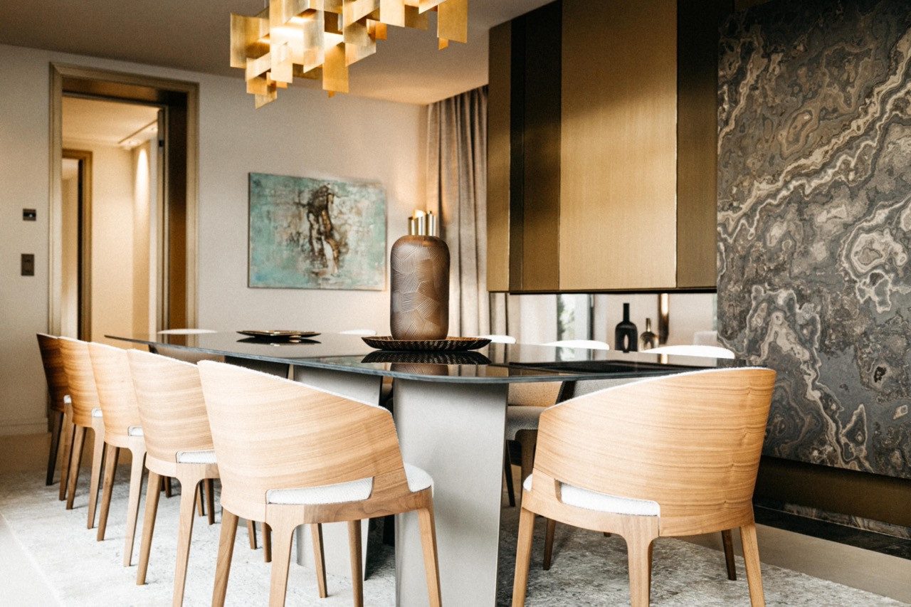 The dining room with curved oak chairs, a black lacquered table and a full-height figured marble wall panel alongside brushed brass cabinetry