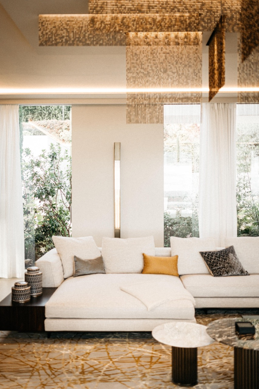 The double-height entrance hall living area with a cream sectional sofa, a gold abstract patterned rug and a large suspended gold mosaic ceiling installation