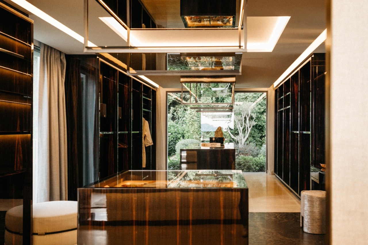 The walk-in wardrobe with Macassar ebony cabinetry, mirrored overhead frame and floor-to-ceiling glazing overlooking the garden