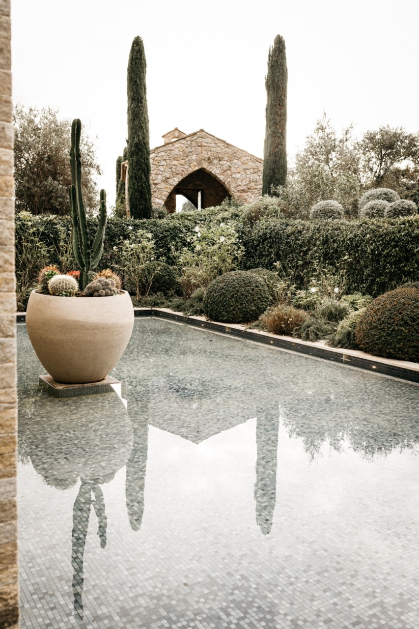 The pool edge with a ceramic cactus planter, the restored stone chapel visible through cypress trees in the background