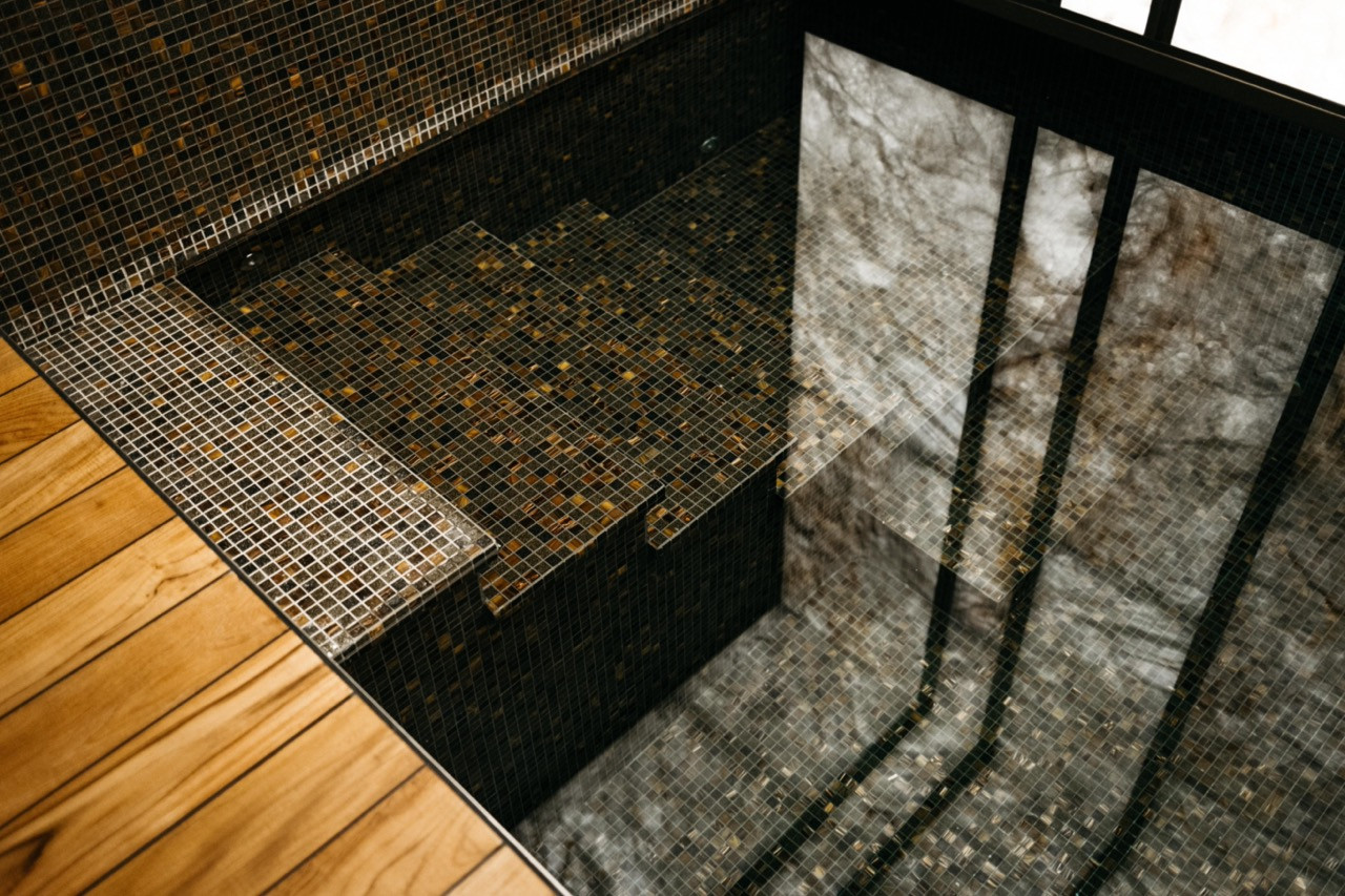 Dark bronze mosaic tiles and marine teak flooring meet at the edge of the basement spa pool