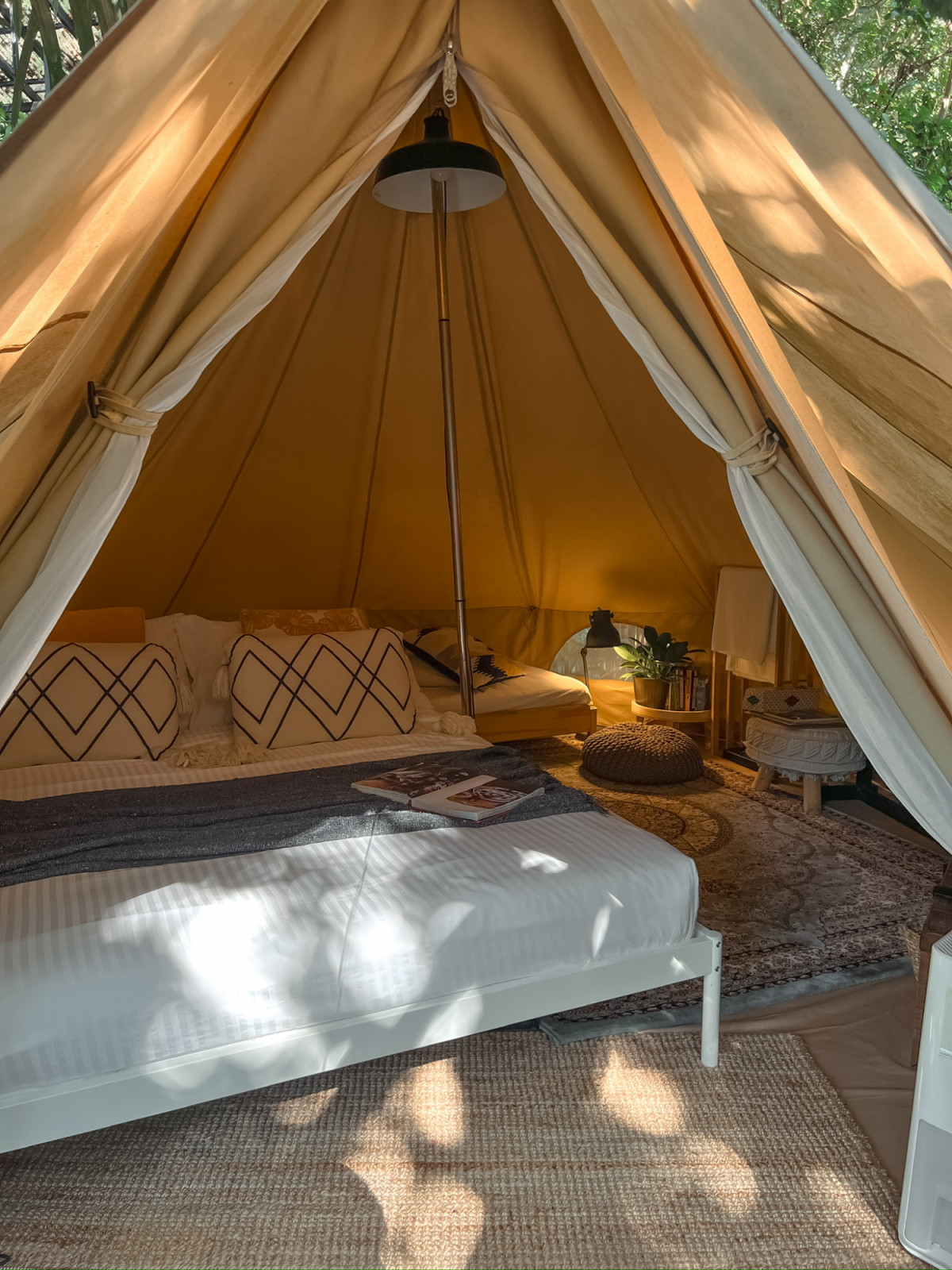 The interior of one of La Hilir's canvas bell tents, with white linen bedding, an Isfahan carpet, and a pendant light suspended from the centre pole