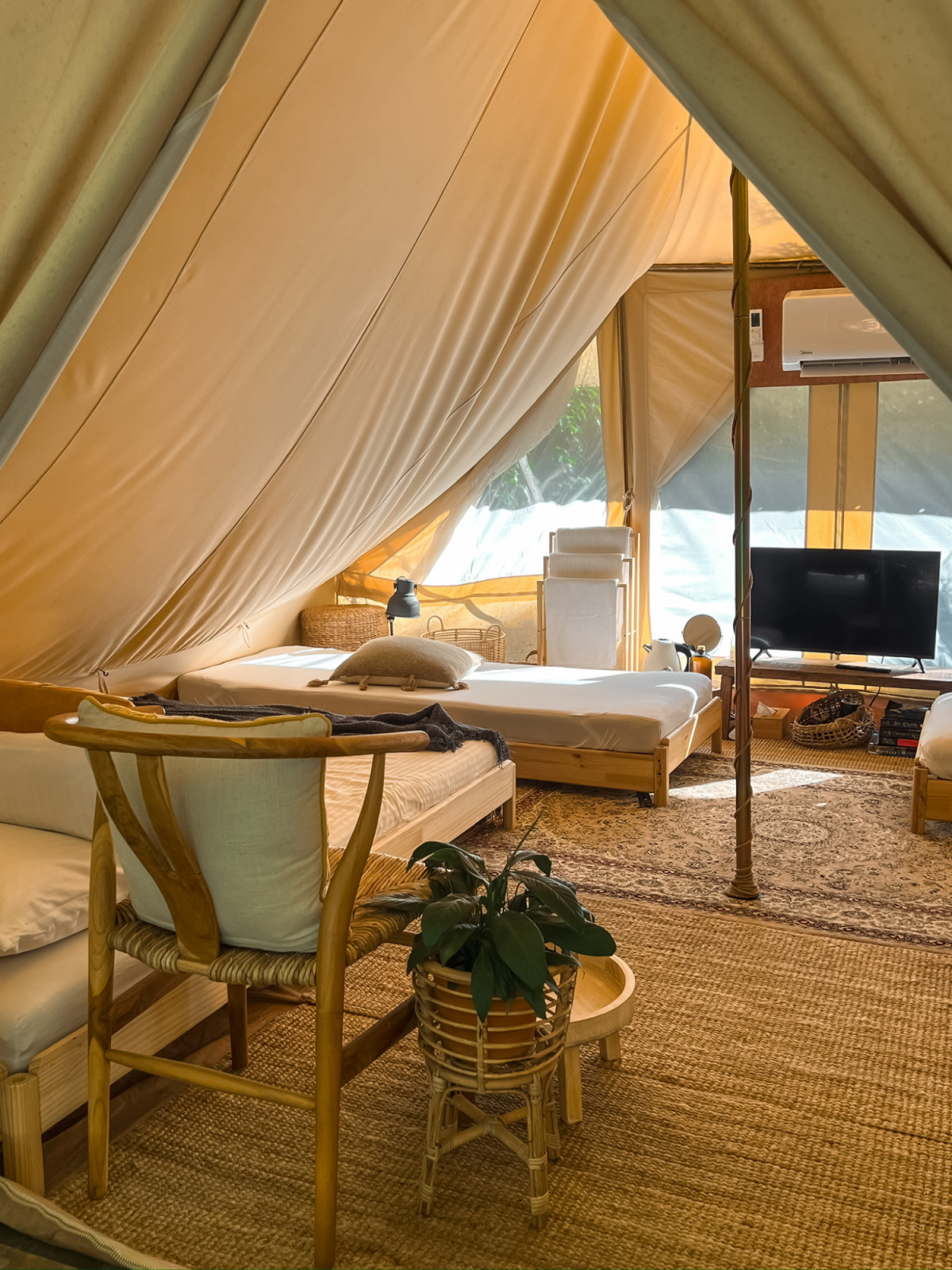 The interior of one of La Hilir’s canvas tents, with twin beds on timber frames, an Isfahan carpet, and a rattan chair beside a small table