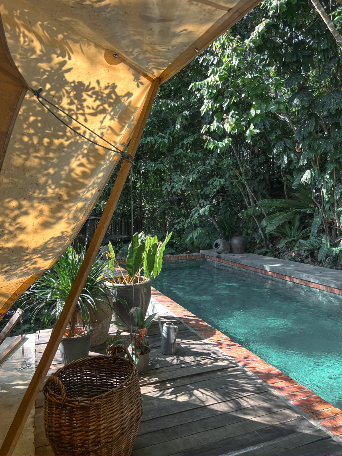The interior of the third tent at La Hilir looking toward the open entrance, with the pool and terracotta brick coping visible through the canvas opening