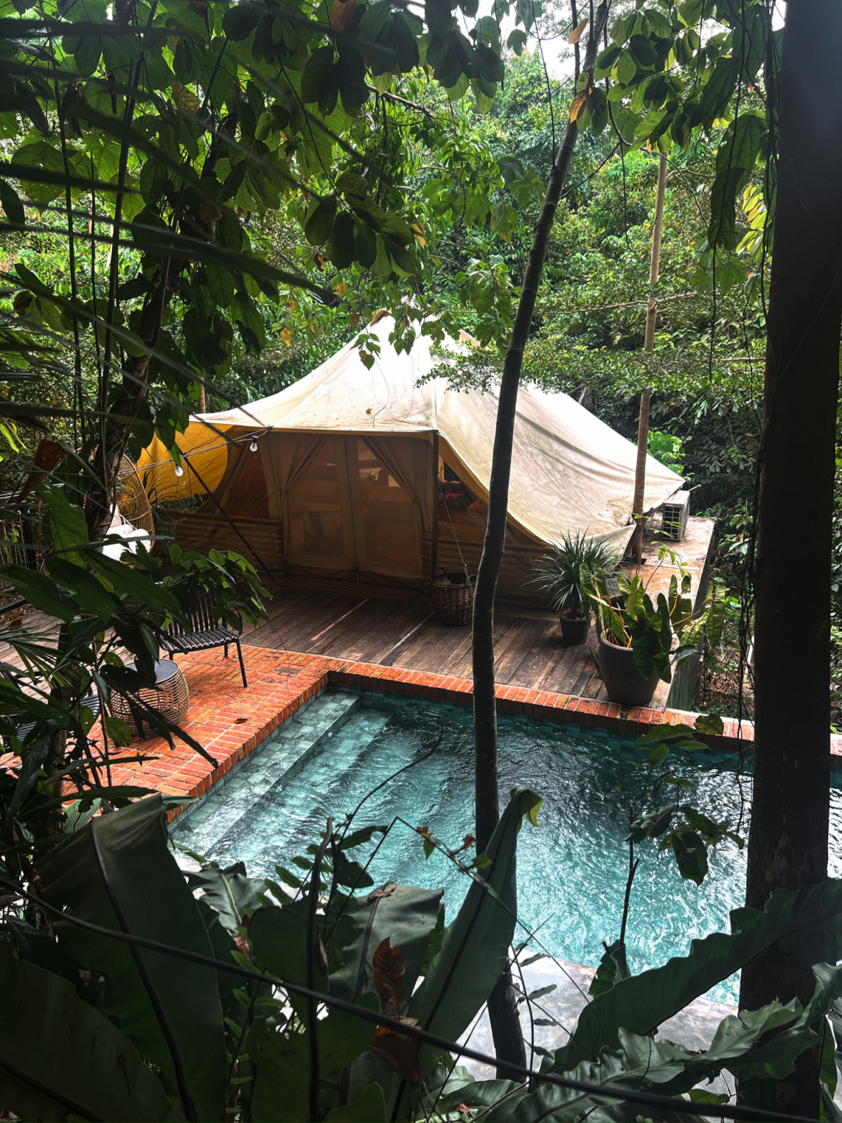 The third tent and pool at La Hilir seen through the tree canopy from the upper terrace, with the timber platform on individual concrete footings visible beneath the canvas structure