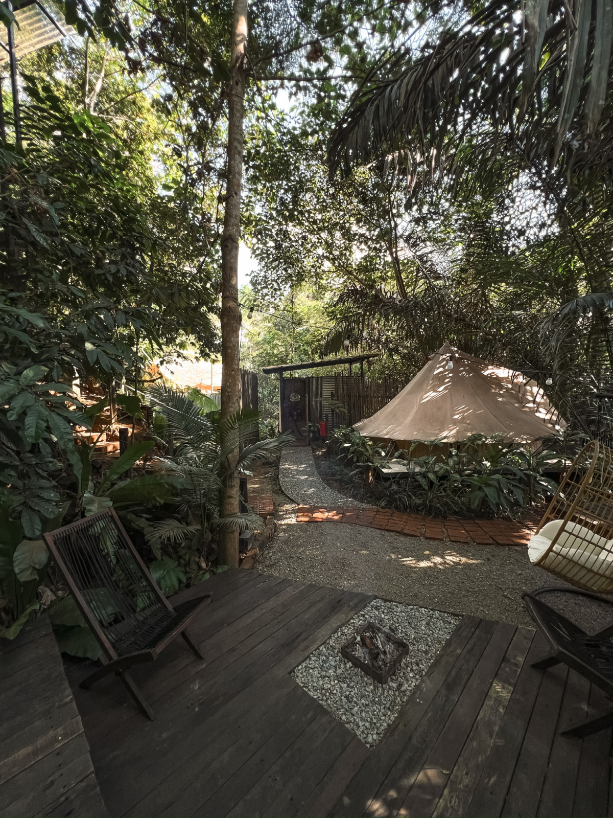 The small recessed firepit set into the deck of the first tent, with a gravel path leading toward the canvas tents and bamboo screen beyond