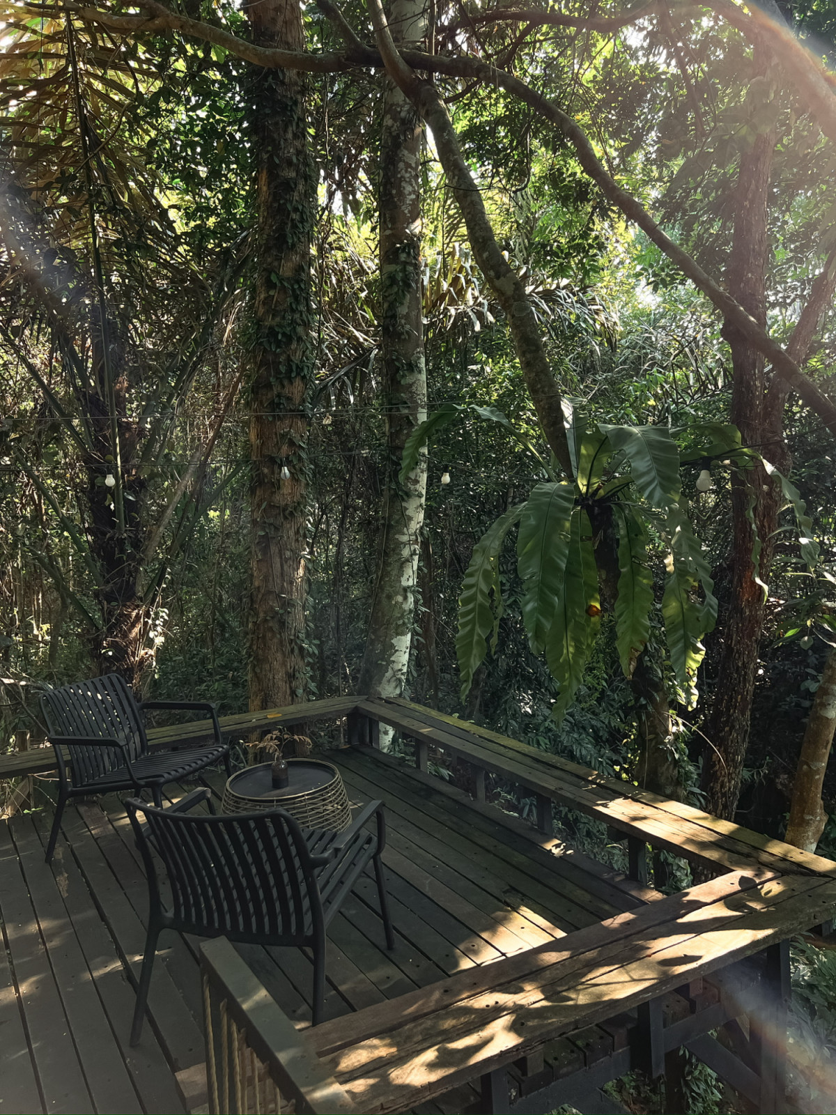 The private deck of one of the upper tents at La Hilir, positioned to face the forest canopy with two chairs and a side table