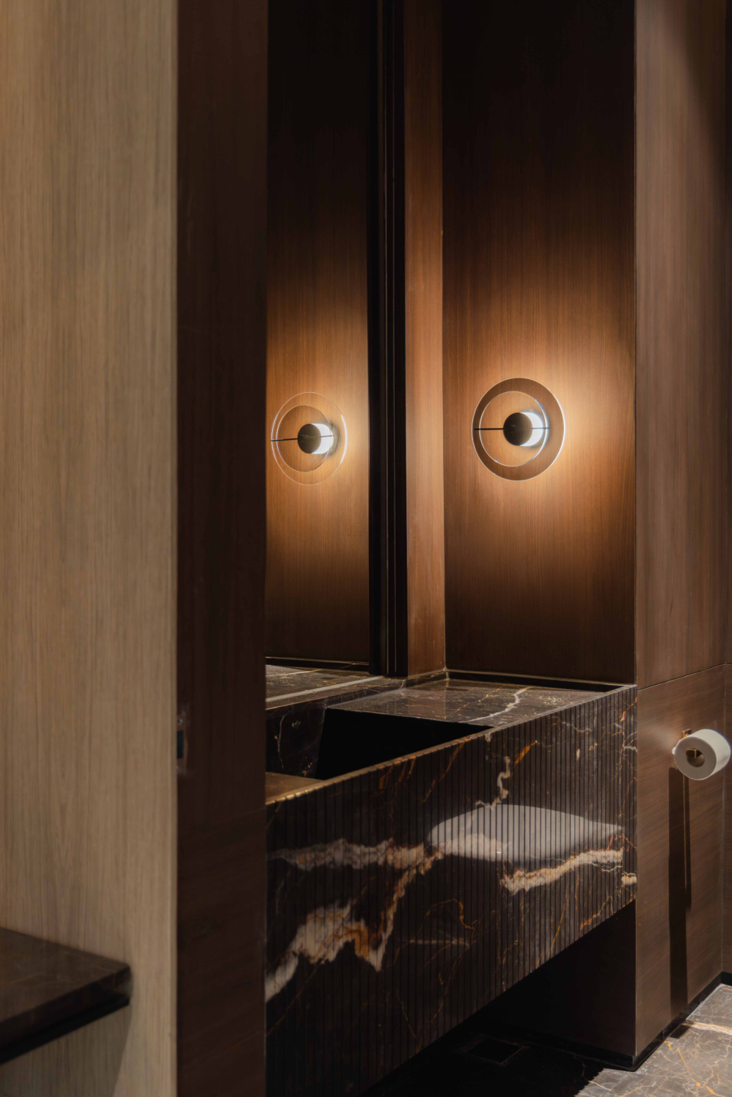 A dramatic powder room features a sculptural dark marble basin and dark timber panelling
