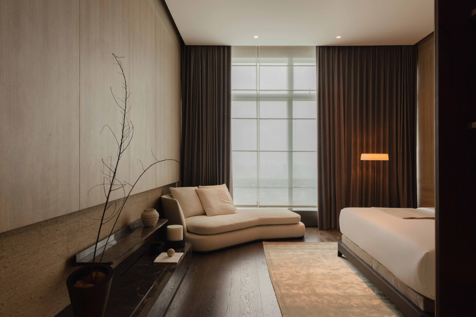 The master bedroom is a composed retreat, with a curved Maxalto chaise, dark timber accents and floor-to-ceiling windows
