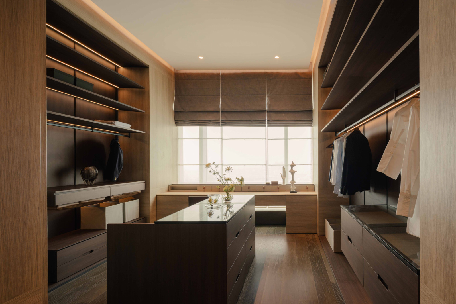 The walk-in wardrobe is finished in dark timber laminate, with a central island that doubles as seating