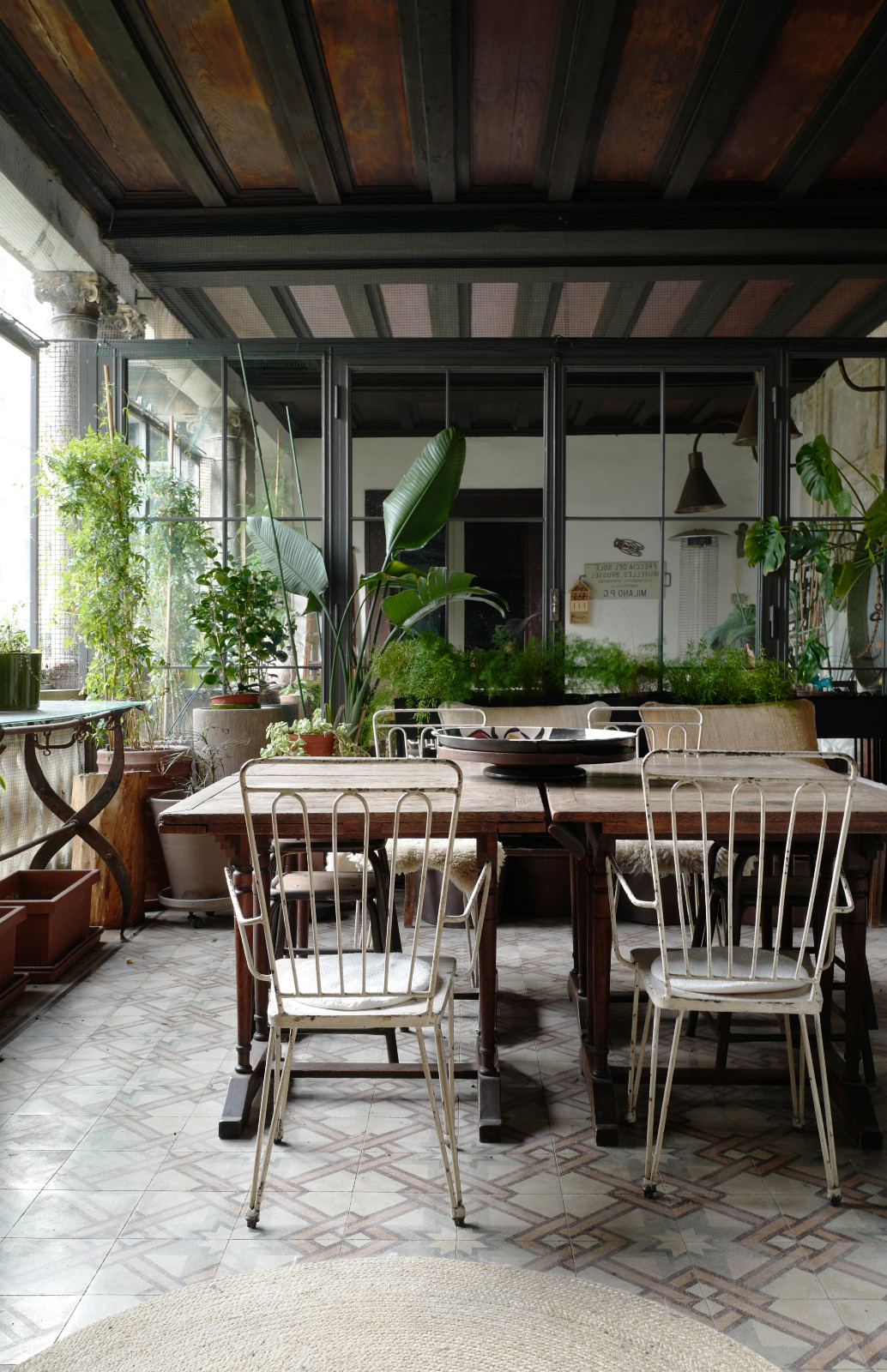 The glass-enclosed terrace blurs the line between indoors and outdoors, where plants, vintage furniture and natural light create a relaxed garden-like retreat
