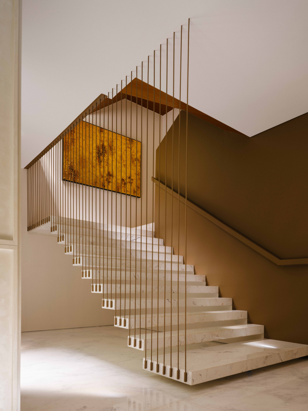 The main staircase ascends through a curtain of slender gold balusters, with a luminous gold artwork anchoring the landing above