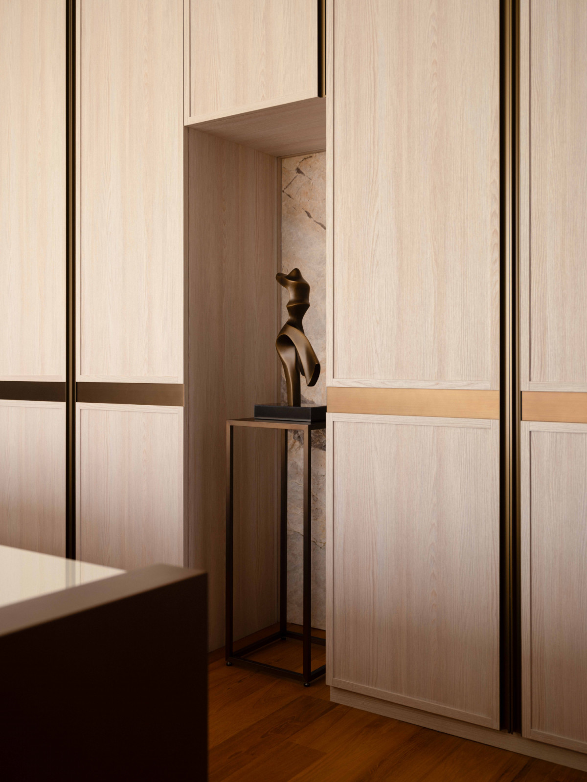 A sculptural bronze figurine occupies a marble-lined display niche carved into the master suite's bespoke wardrobe wall