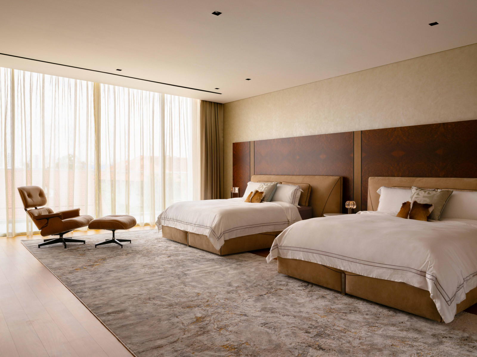The master bedroom pairs two Visionnaire queen-size beds against an exotic burl wood timber feature wall, with an Eames lounge chair positioned by the window