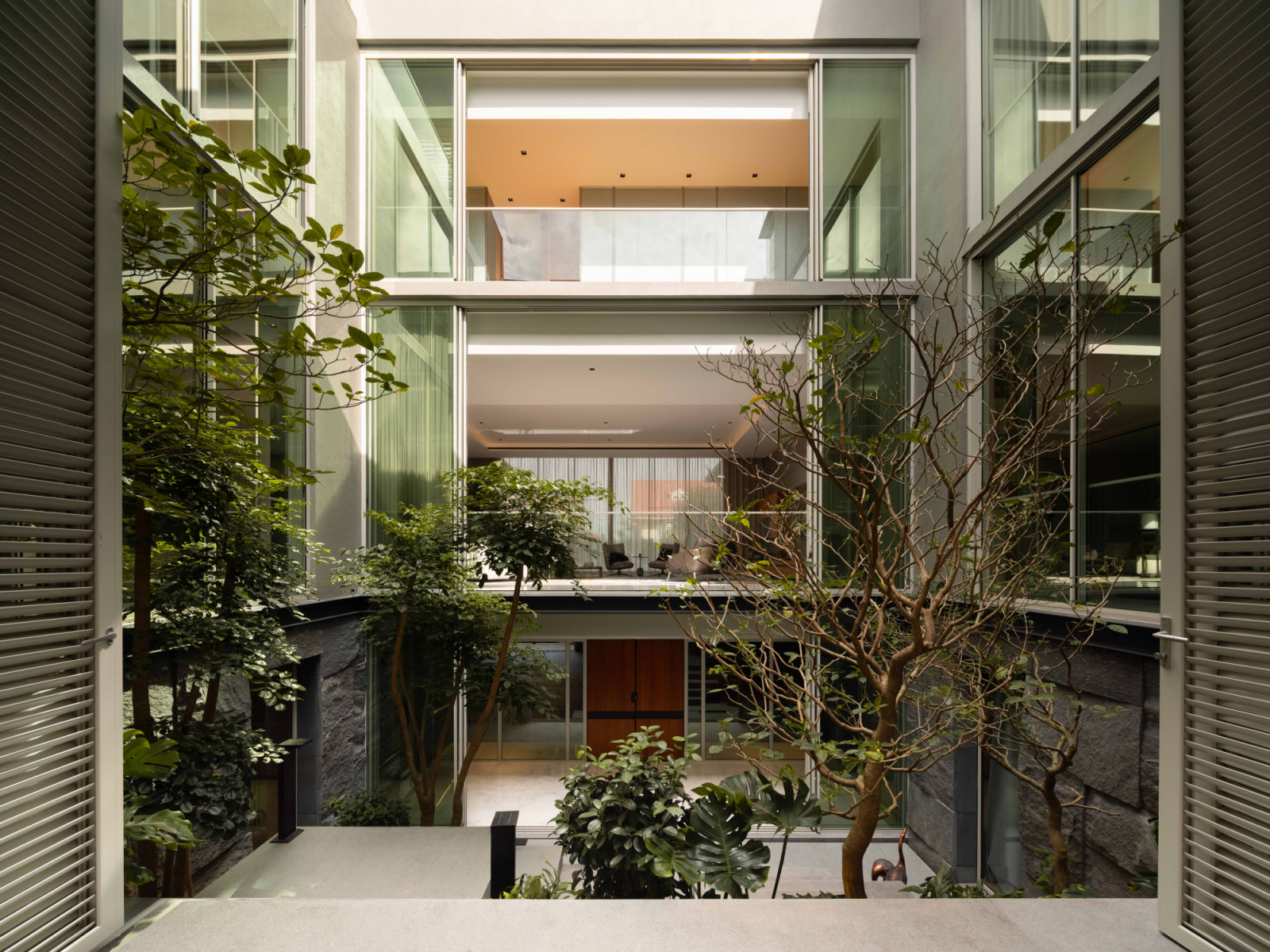 The verdant central courtyard, framed by full-height glazing across all levels, forms the beating heart of the bungalow named Within The Walls House