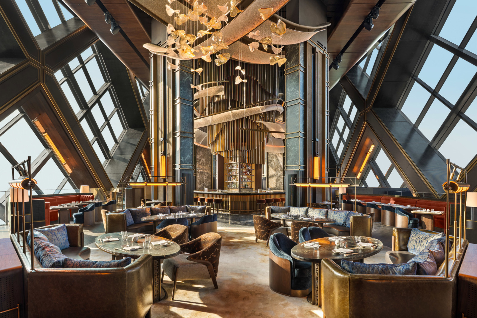 The main dining room at Nobu One Za’abeel, designed by Rockwell Group, with the sky concourse’s crisscrossing geometric glazing framing the space and a custom chandelier of amber glass forms suspended above (Photo: Alex Jeffries)