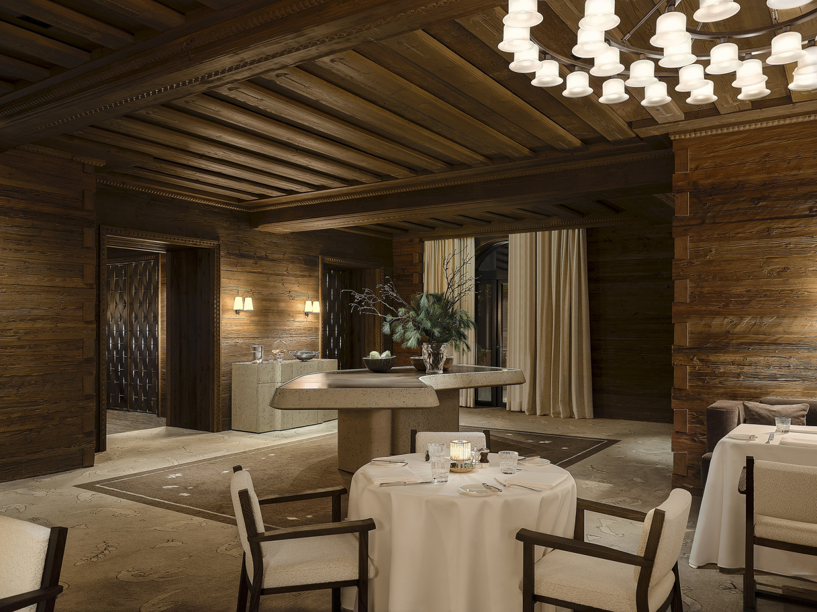 The main dining room at Monti, with its exposed timber beam ceiling hung with a circular cluster of glass pendant lights, a stone service credenza at the centre and the woven bronze room dividers visible through the doorway (Photo: Giulio Ghirardi)