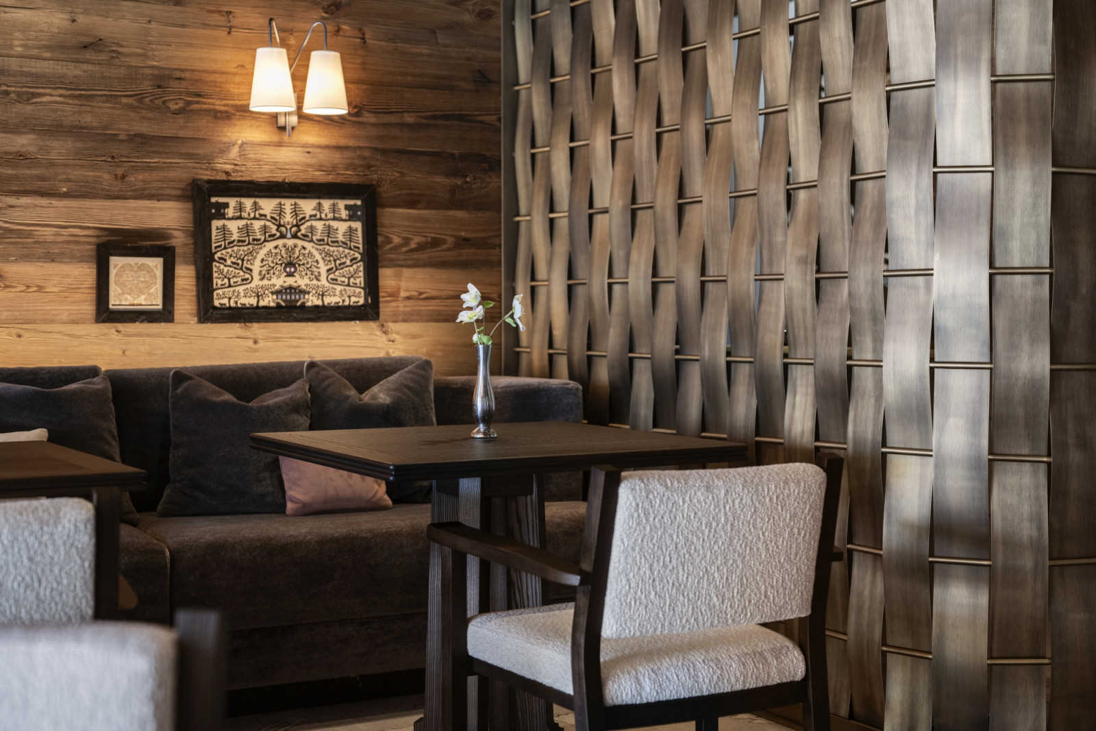 A dining nook at Monti showing the woven bronze room divider that references basket-weaving techniques, alongside a mohair banquette, folk art on the timber wall and a boucle dining chair (Photo: Giulio Ghirardi)
