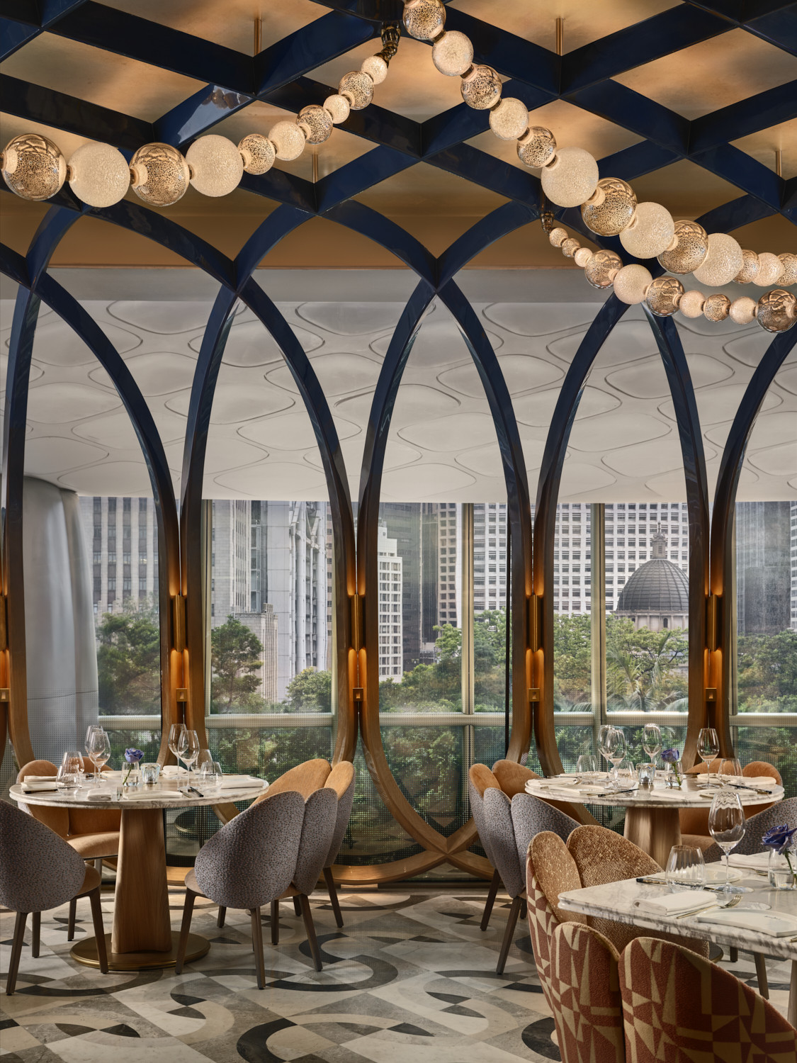 The perimeter dining area of Akira Back Hong Kong by day, with a row of timber-framed arches framing views over Hong Kong’s Central district, a geometric terrazzo floor and a string of globe pendants running the length of the ceiling (Photo: Owen Raggett)