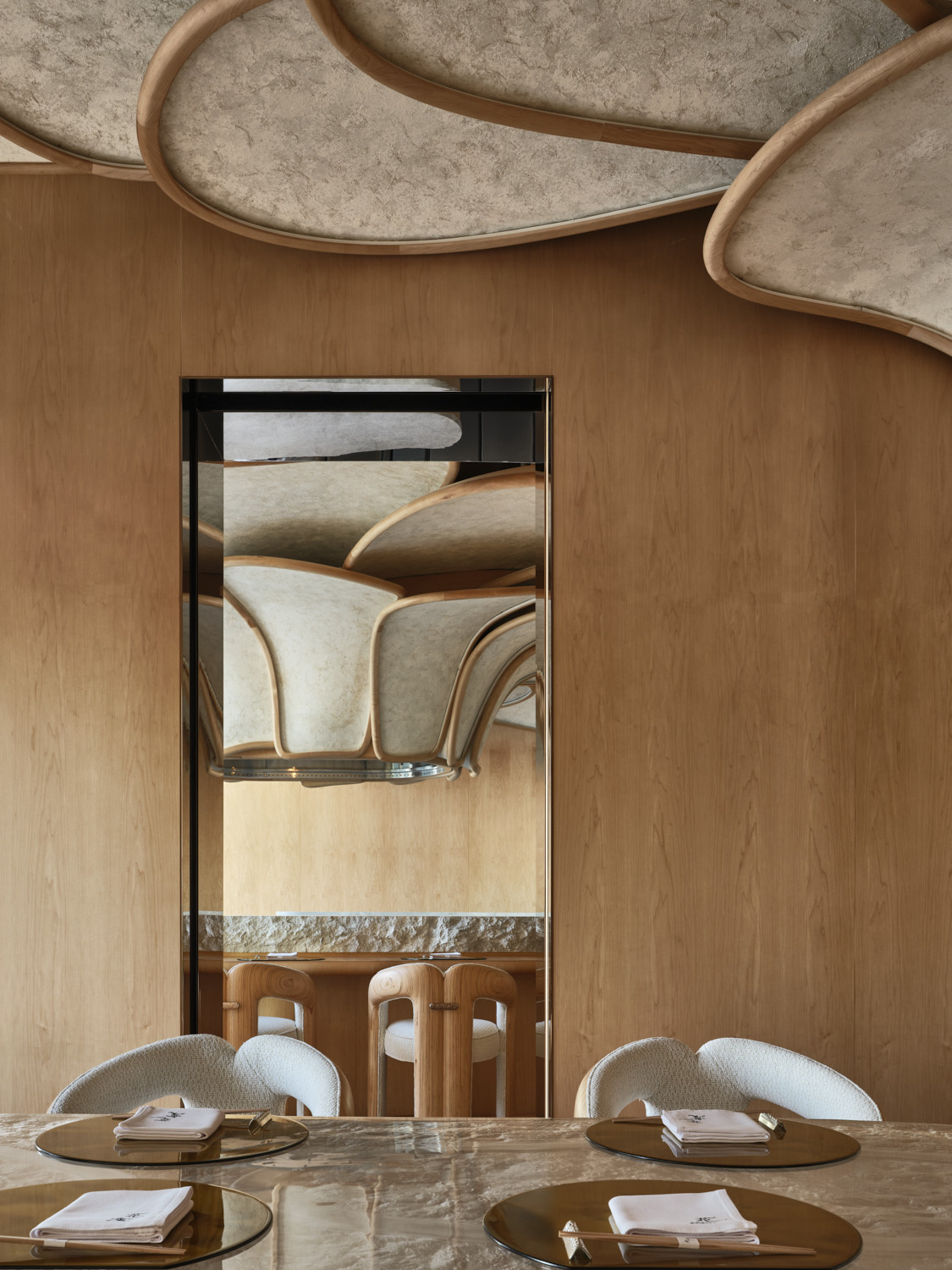 A view from the private dining room into the kappou counter through a brass-framed mirror, reflecting the petal ceiling installation and the cedar stools at the counter beyond (Photo: Owen Raggett)