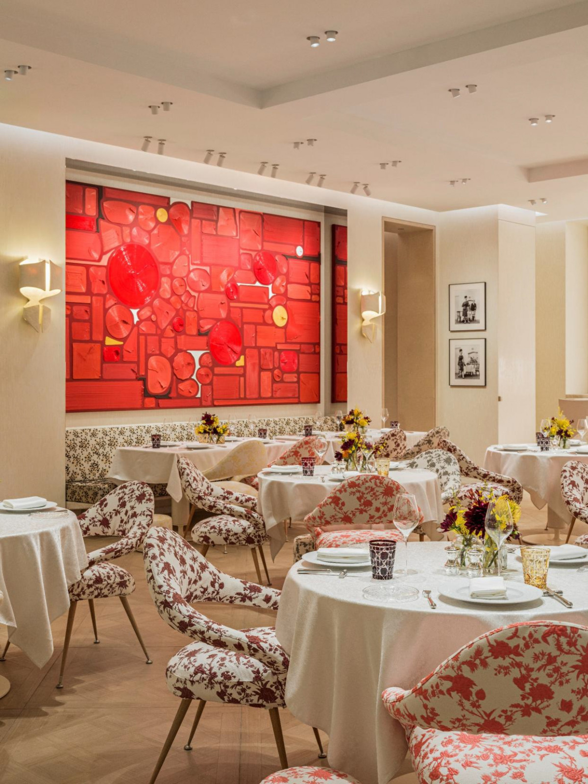The main dining room shows a large red relief artwork by Hong Hao on the end wall, with floral-upholstered chairs in two colourways and black-and-white Dior archive photographs hung to the right
