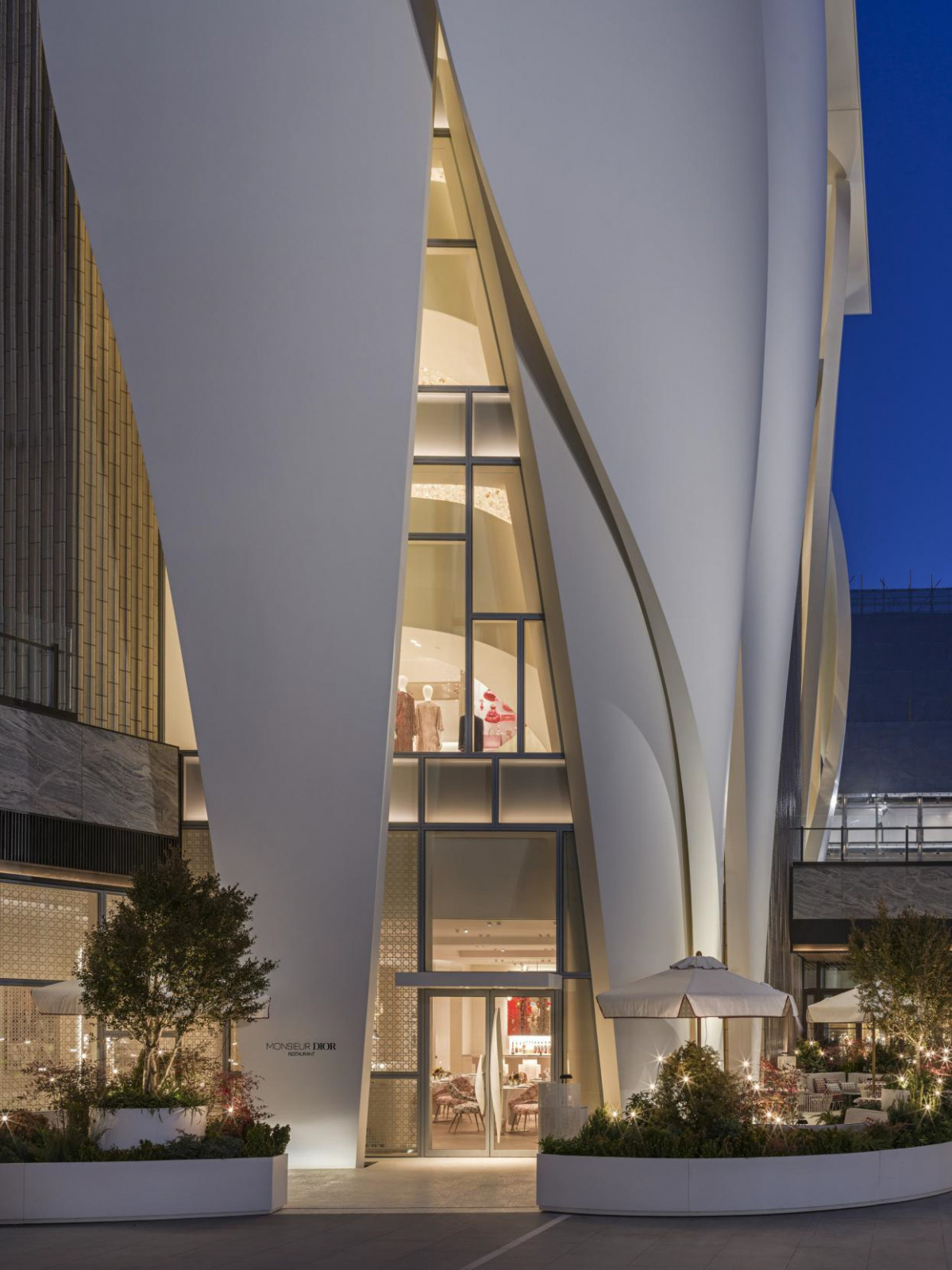 The exterior entrance to Monsieur Dior by Anne-Sophie Pic within the House of Dior Beijing in Sanlitun, its sculptural white facade designed by Christian de Portzamparc visible above the ground-floor terrace