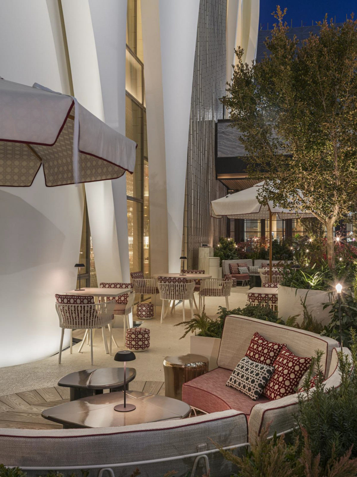 The outdoor terrace at Monsieur Dior by Anne-Sophie Pic, furnished with cane-patterned chairs and cushions in Dior’s signature cannage motif, is set between the curved white volumes of Christian de Portzamparc's building