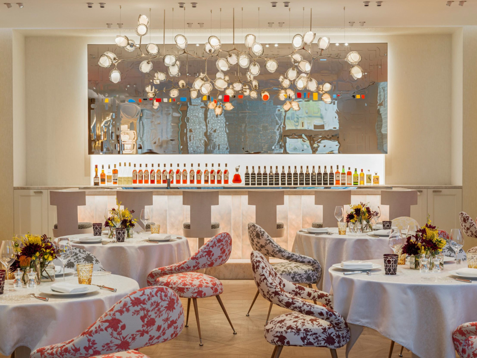 The dining room at Monsieur Dior by Anne-Sophie Pic, Beijing, with floral-print chairs in Dior toile, a branching chandelier and a work by Chinese artist Hong Hao on the mirrored bar wall behind