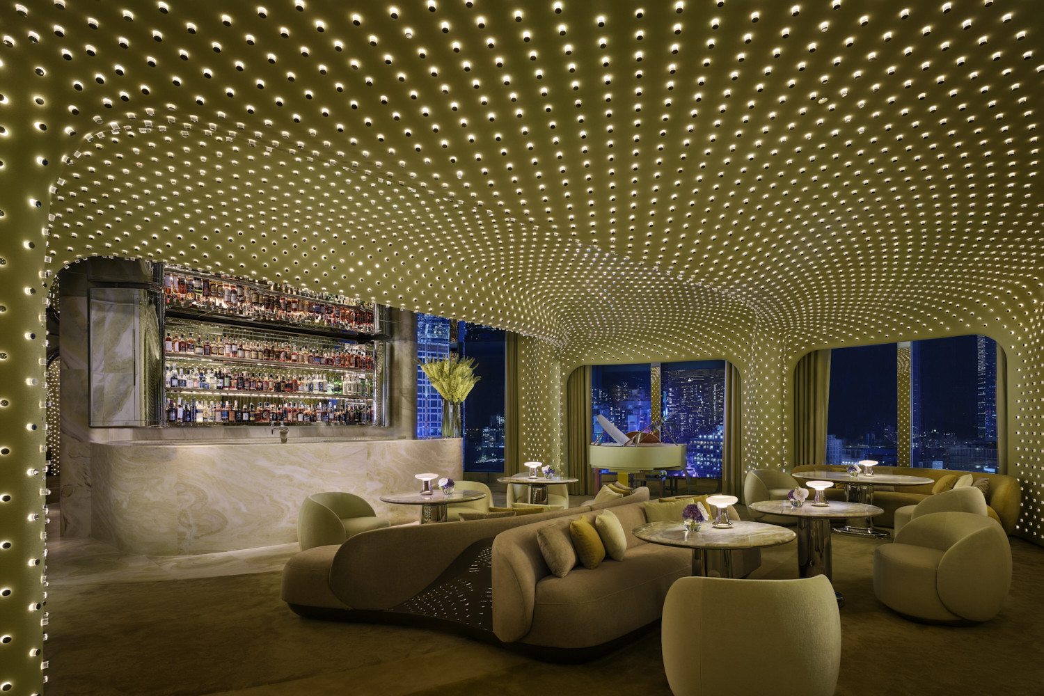 Peridot after dark, looking towards the marble bar set into the lit wall surround, with the city skyline visible through arched windows and the full extent of the 20,000-light installation illuminated across the ceiling and walls