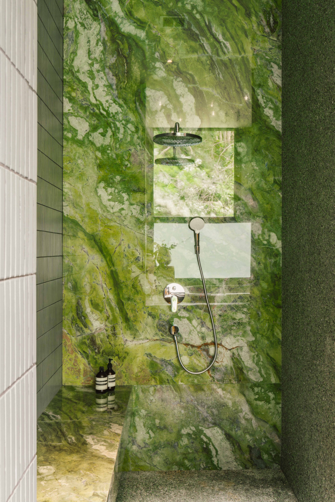 The vibrant emerald tones of the large-format tiles in the shower area echo those of the greenery outdoors