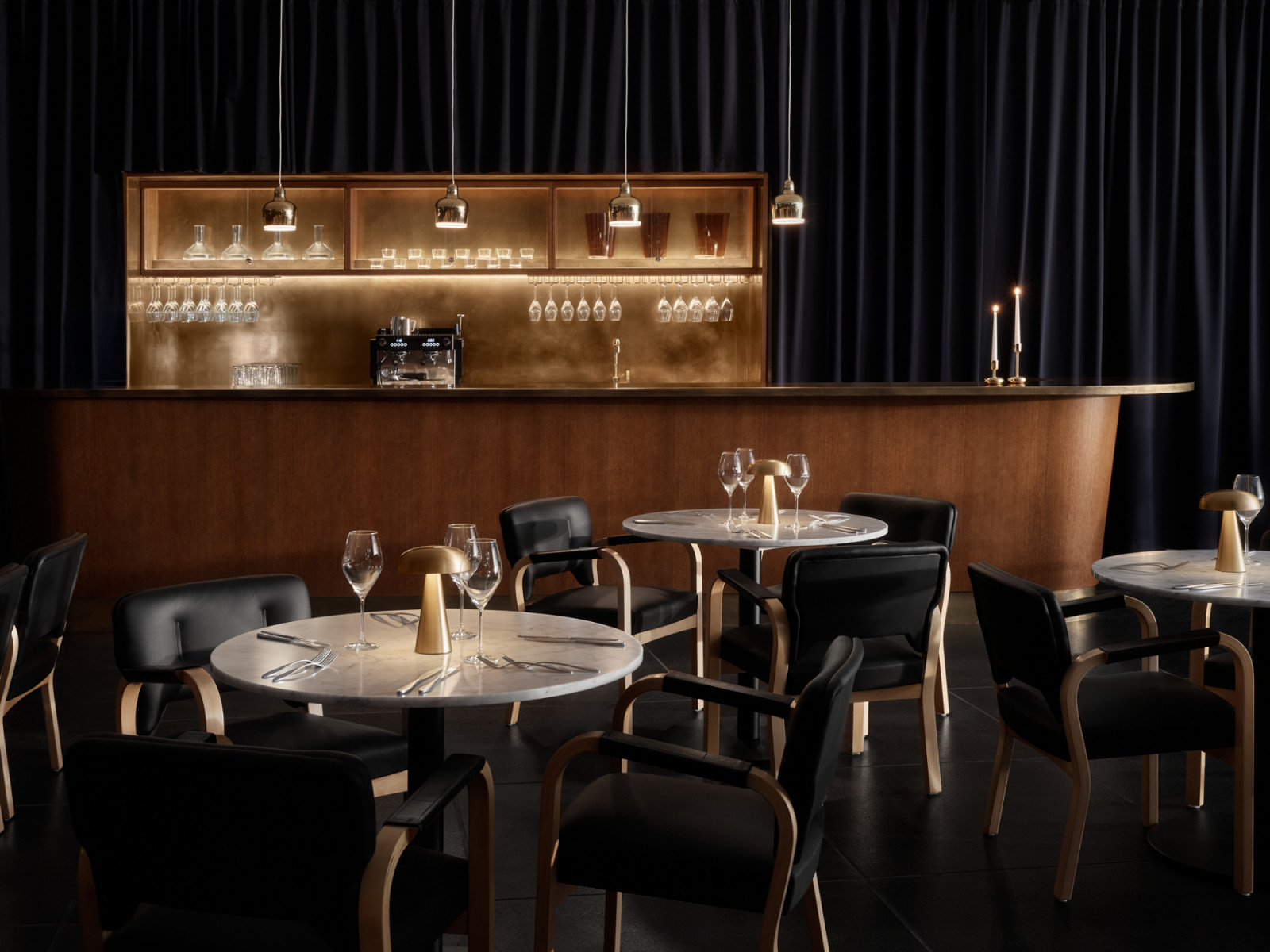 The bar area at Finlandia Bistro, its curved walnut counter set against floor-to-ceiling navy curtains, with a brass-backed display shelf, new bespoke pendants and original Aalto chairs in the foreground