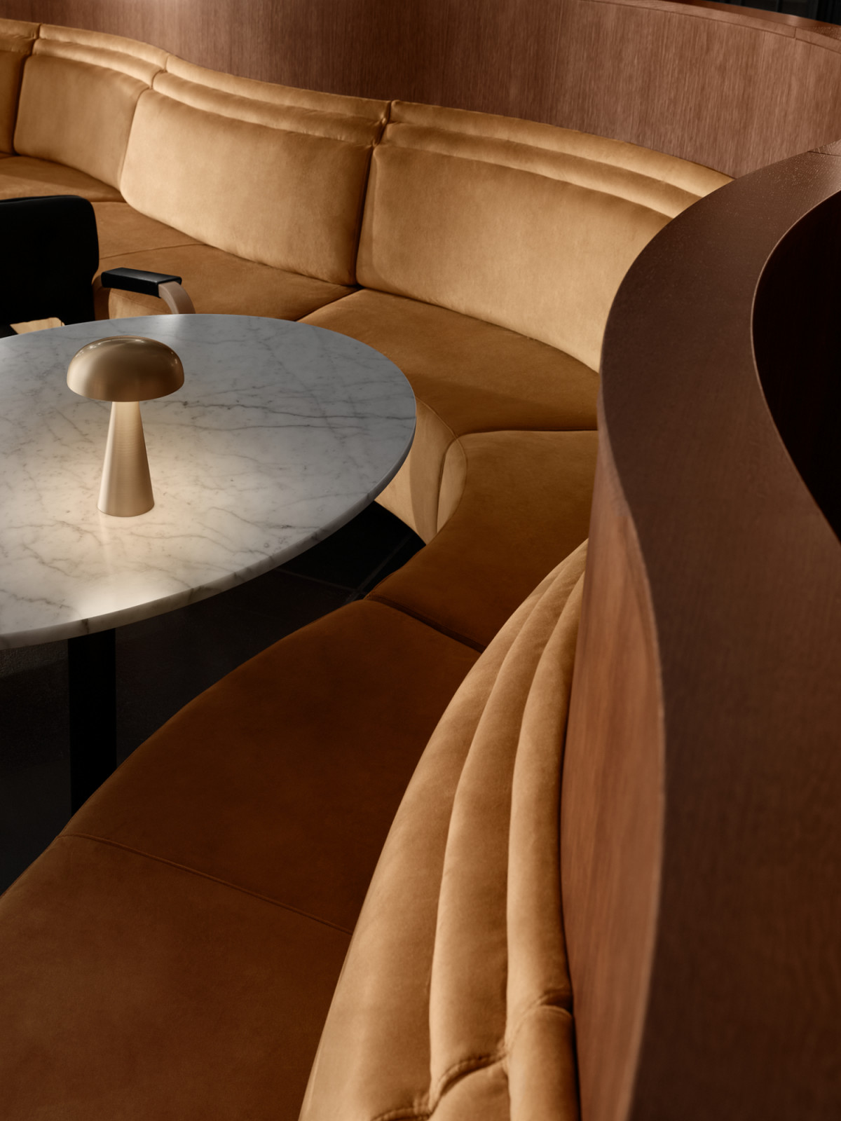 A close detail of one of Fyra's new bespoke circular banquettes in caramel velvet, set alongside a marble-topped table with a brass mushroom lamp, the walnut wall panelling of Finlandia Hall visible behind