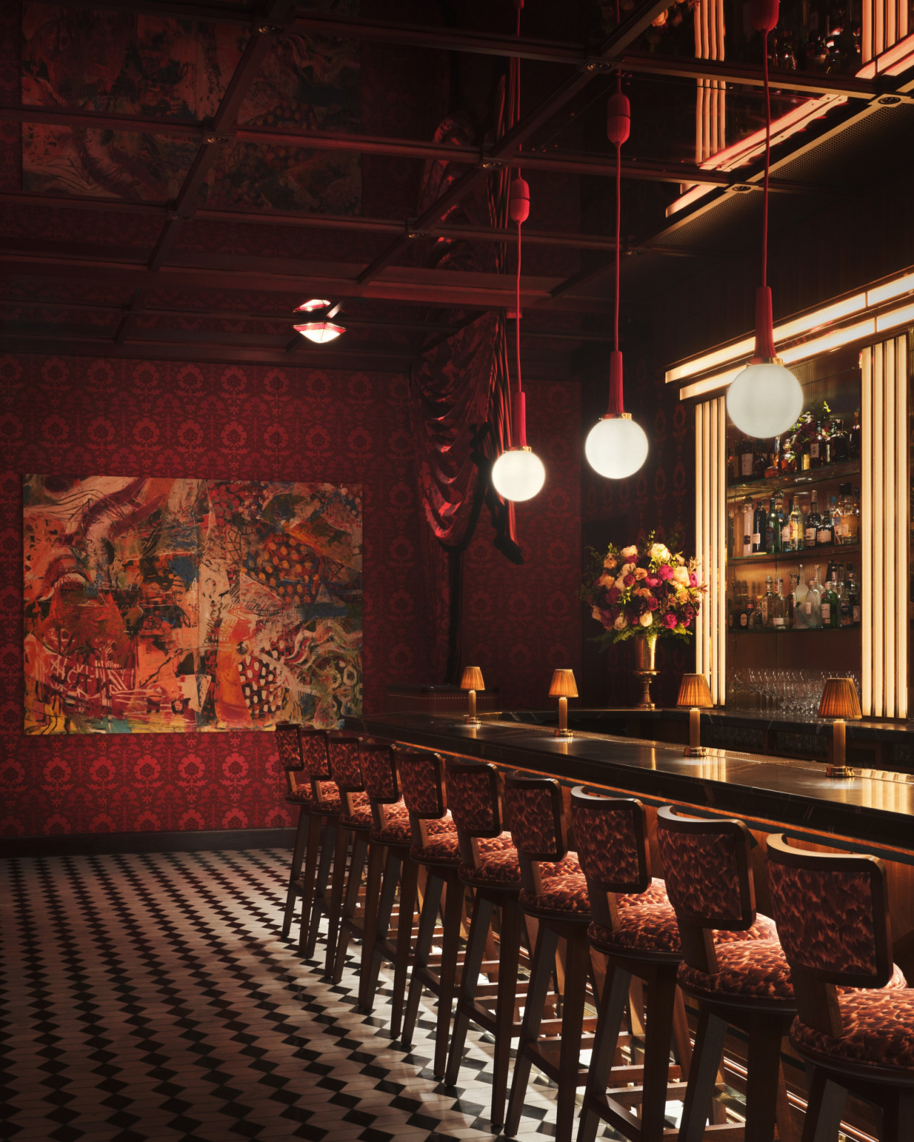 The lower-level bar at Carbone London, its red damask walls hung with a large abstract painting, barstools in matching patterned fabric running the length of a black marble counter, with globe pendants and a chequered floor
