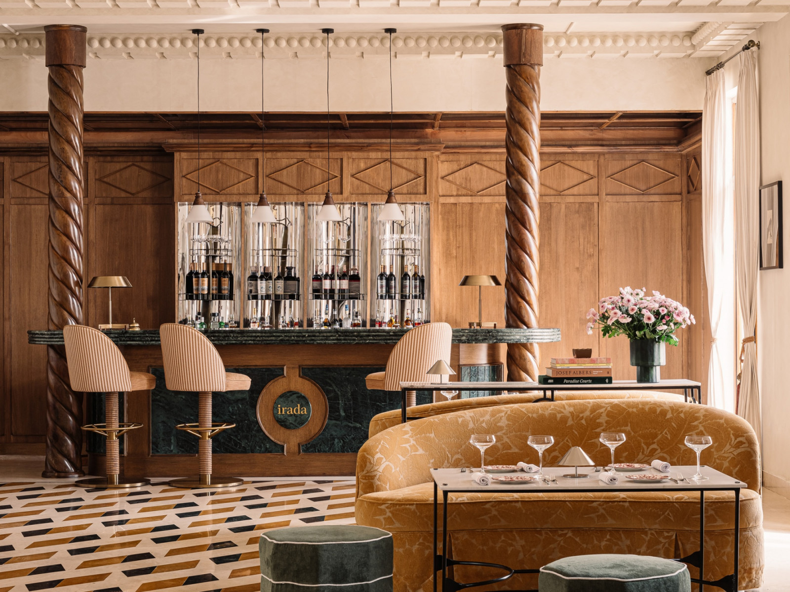 The bar at Rosso within Hotel Irada, its green marble counter flanked by two Solomonic columns of polished wood referencing Italian Baroque, with striped bar stools, a panelled back bar and a geometric marble floor (Photo: Ishi Sitwala)