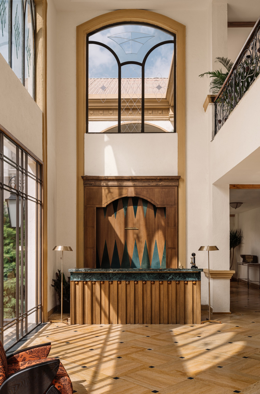 The entrance lobby of Hotel Irada, designed by Humming Tree, with a double-height arched window, a green marble and timber reception desk with teal geometric inlay and a parquet floor with diamond detailing (Photo: Ishi Sitwala)