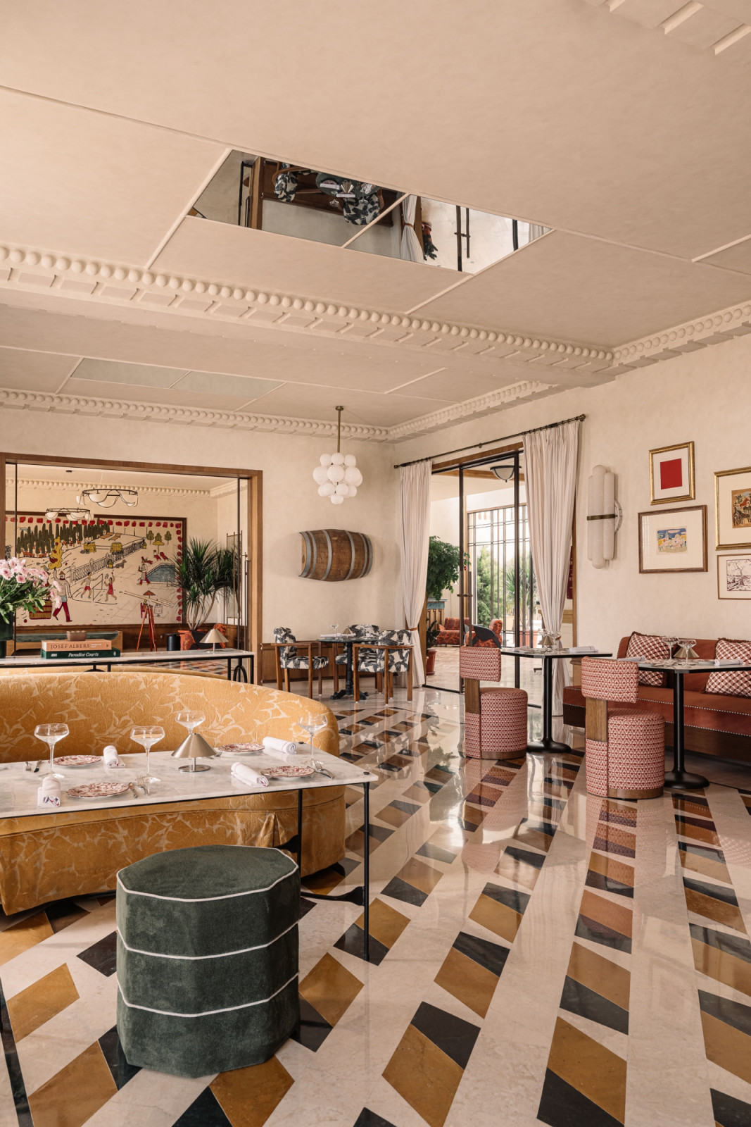 The dining room at Rosso, with a bold geometric polychrome marble floor, a gold jacquard curved banquette, plasterwork cornicing and a mirror inset into the ceiling, with a wine barrel and artworks on the walls beyond (Photo: Ishi Sitwala)