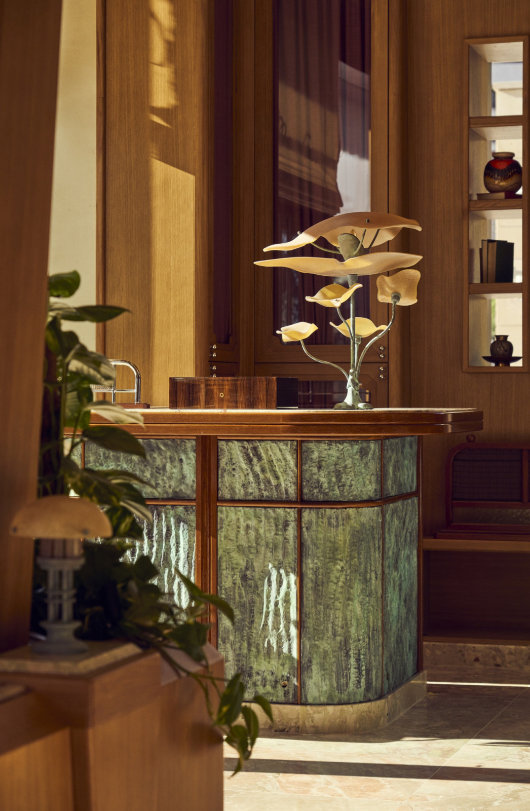 The sculptural central bar at Marlow, its curved base clad in green patinated panels with a timber surround, topped with a branching metal table lamp in the form of stylised leaves (Photo: Alexandre Tabaste)