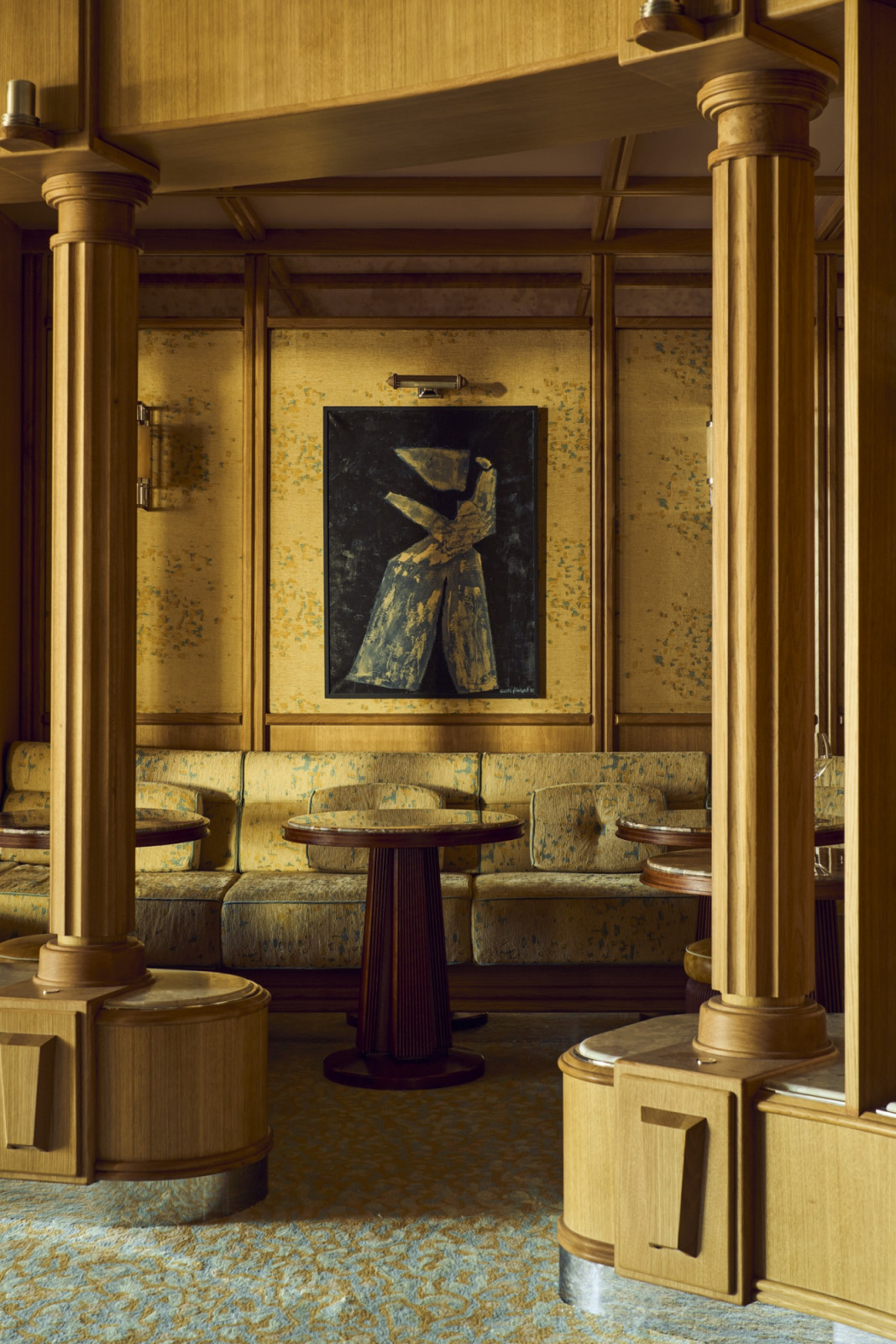 A lounge alcove at Marlow framed by timber columns, with yellow-green textured banquette seating, a ribbed pedestal table and a figurative painting hung on the textured wall panel between the columns (Photo: Alexandre Tabaste)