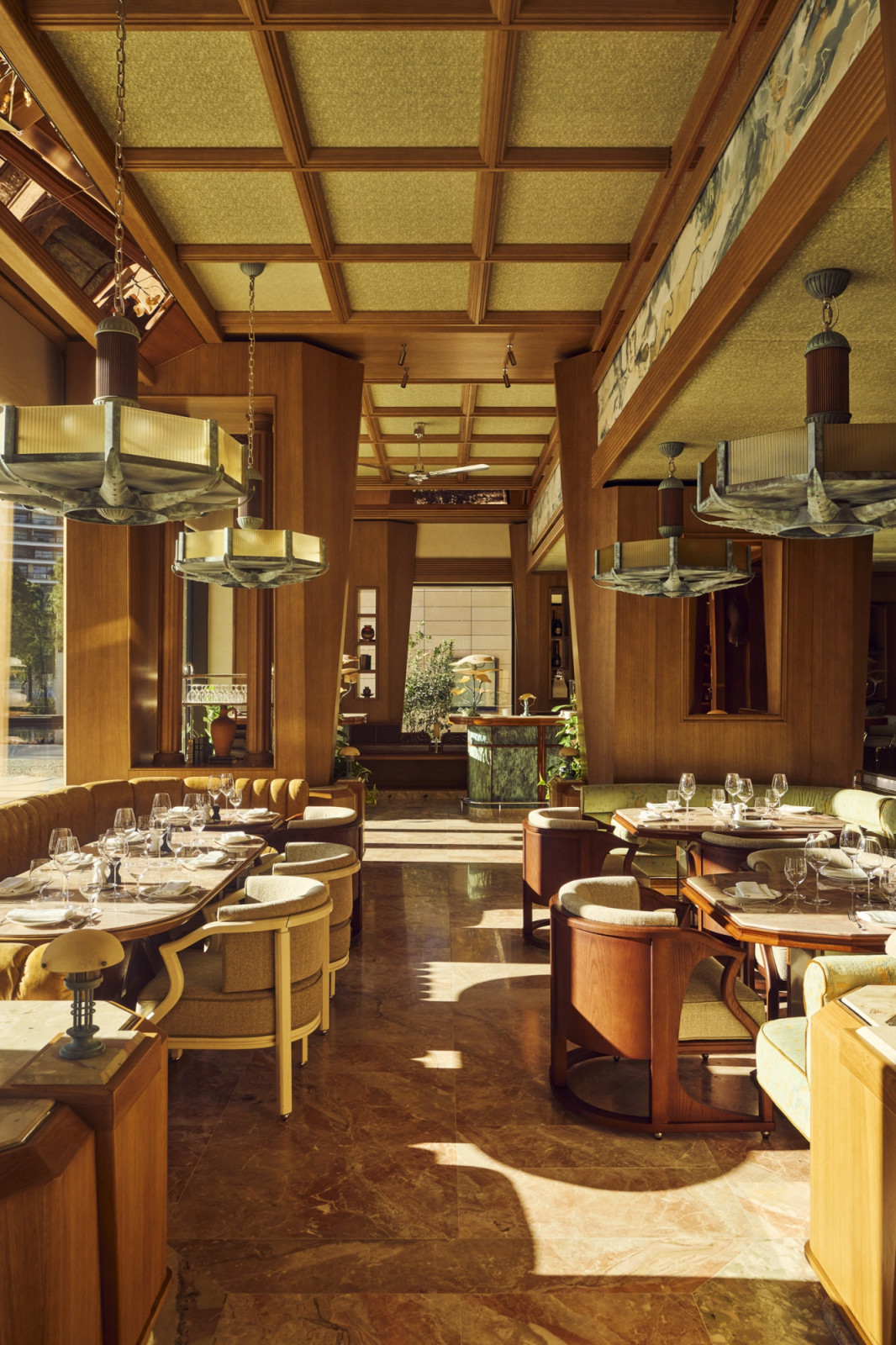 The main dining room at Marlow, Monaco, designed by Hugo Toro, with a coffered timber ceiling, custom tiered pendant lights, upholstered banquettes in olive and gold, and a painted frieze running the length of the upper wall (Photo: Alexandre Tabaste)