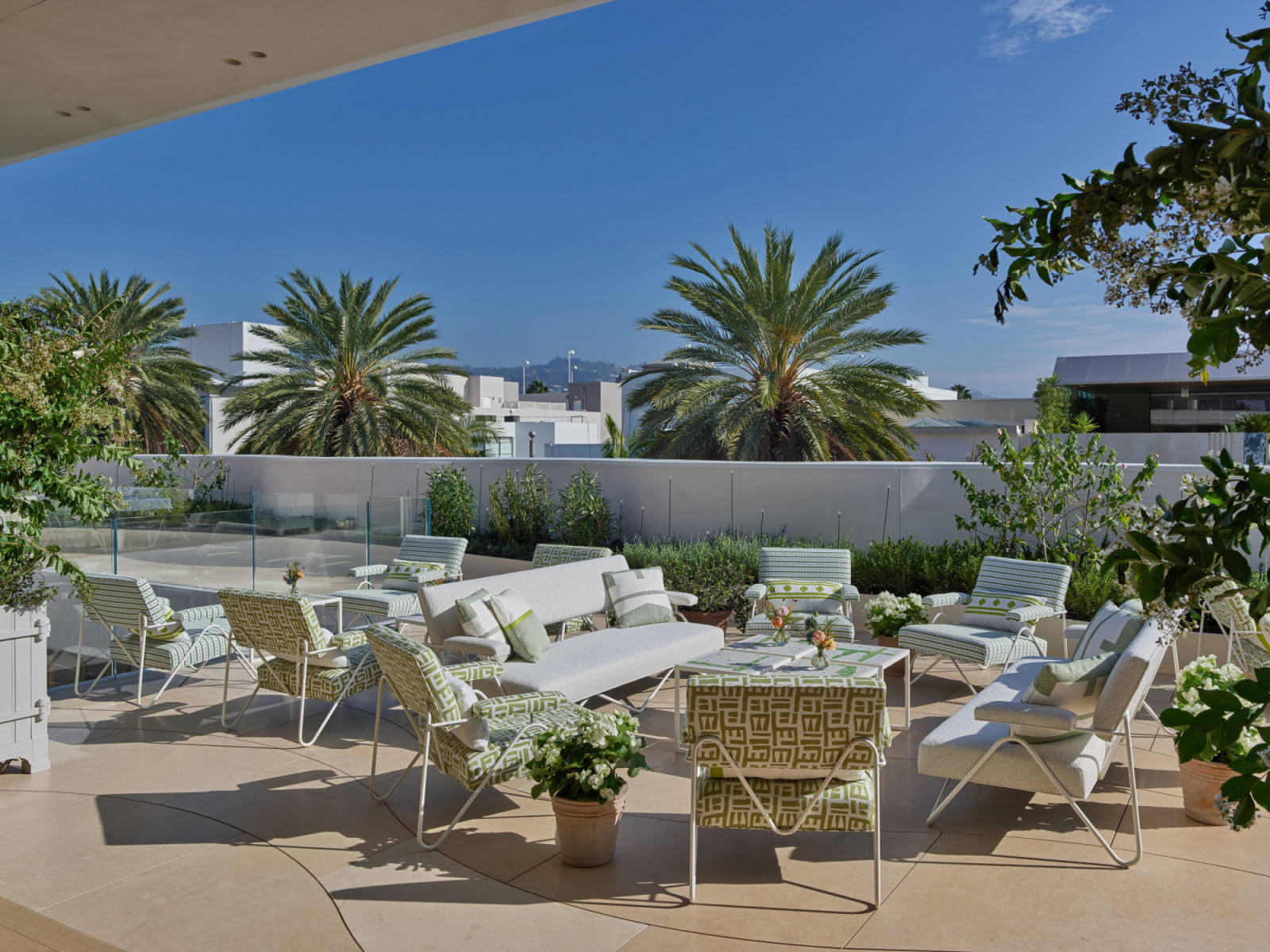 The outdoor terrace at Monsieur Dior by Dominique Crenn, Beverly Hills, designed by Peter Marino, with green and white patterned garden furniture, planted borders and palm trees overlooking Rodeo Drive