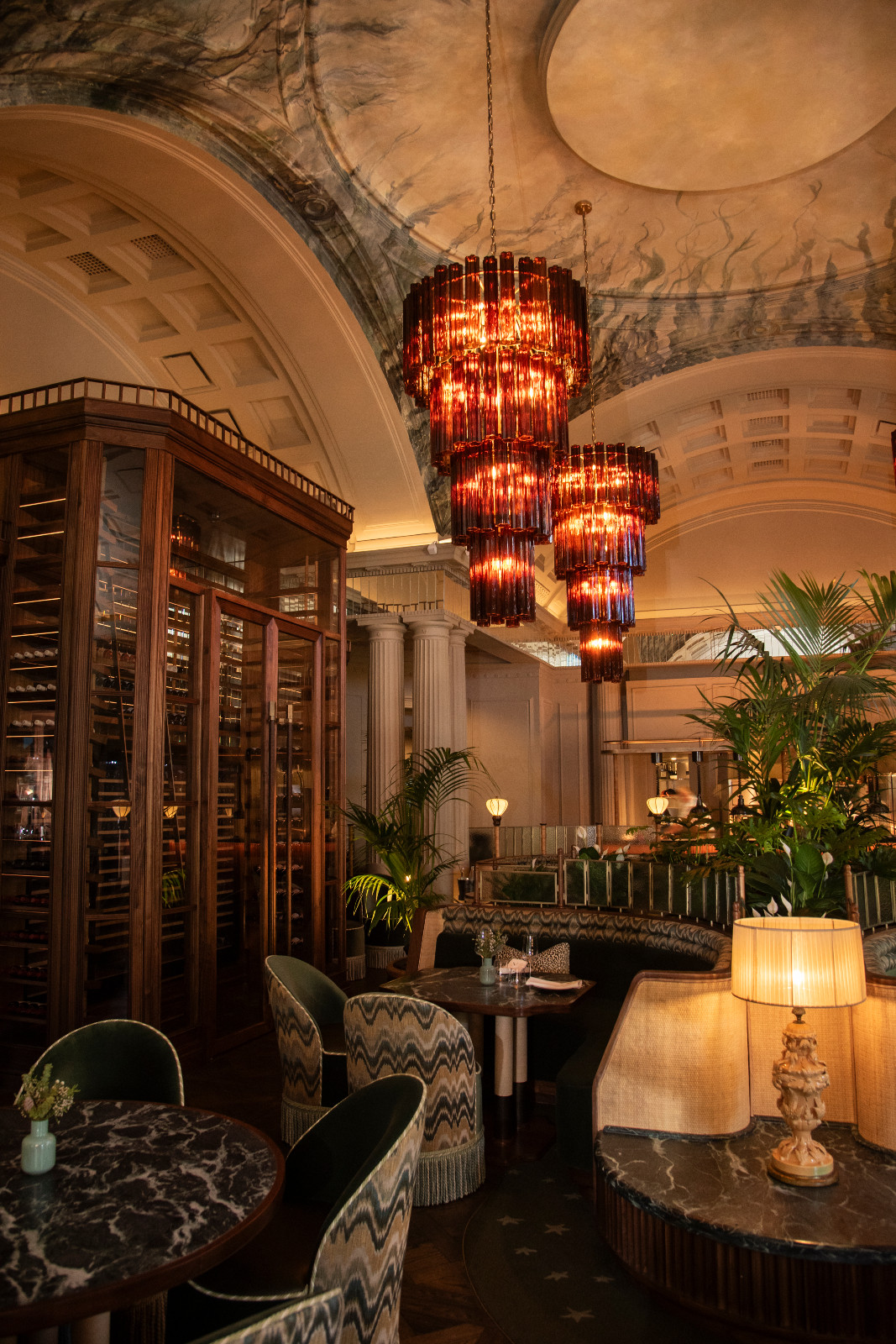 A dining area at Amura by Ángel León, Cape Town, designed by Tristan du Plessis, with amber glass tiered chandeliers suspended beneath a vaulted ceiling painted with marine imagery, a floor-to-ceiling wine cabinet and ikat-upholstered chairs (Photo: Claire Gunn)