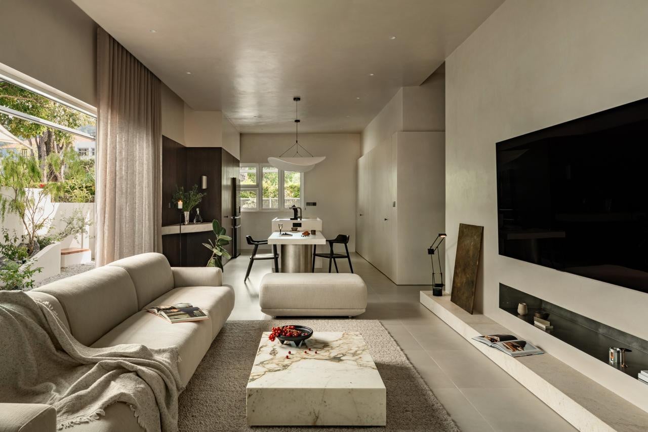 A view from the living room through to the dining area, where a limestone-topped table on a brushed steel cylinder base sits beneath a white sculptural pendant