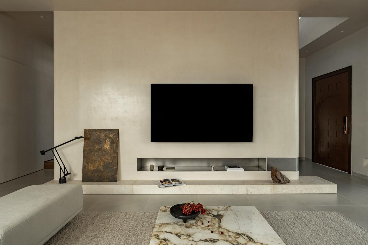 The textured plasterwork TV wall with its recessed steel ledge, limestone plinth, and found driftwood; the Artemide Tizio lamp rests to the left