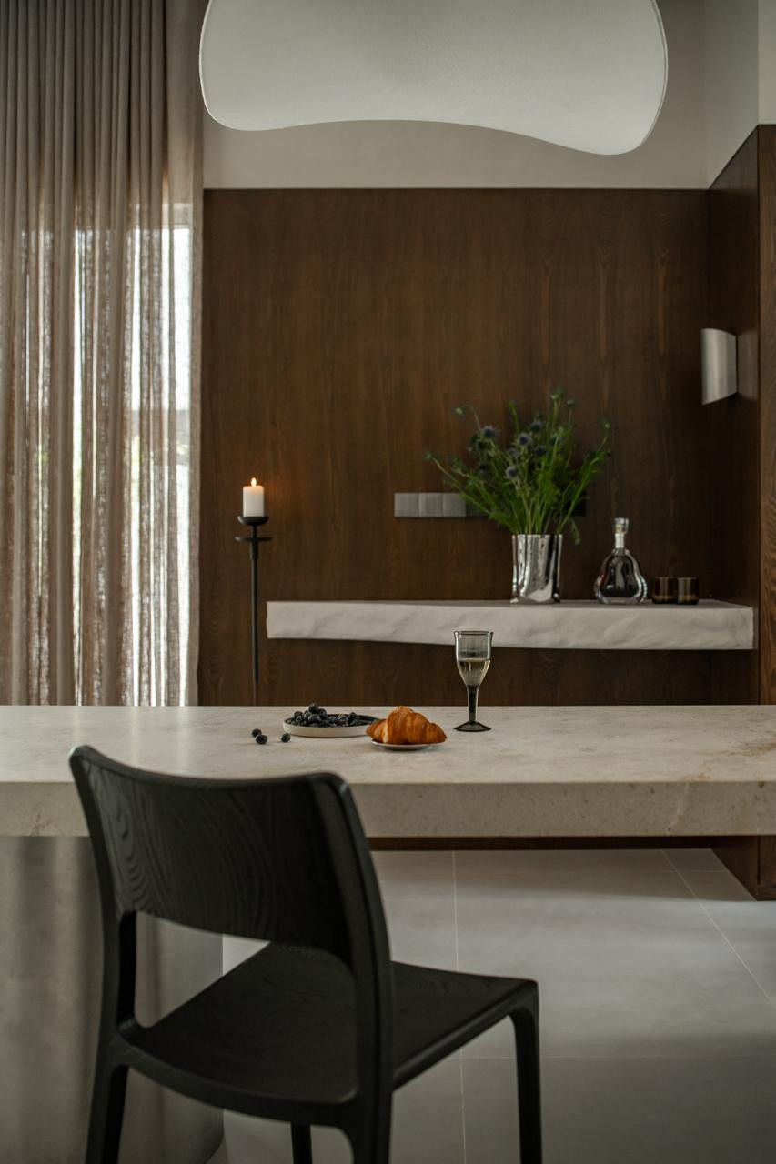 Looking across the limestone dining table towards the floating stone console, styled with dried thistles in a faceted silver vase and a glass decanter