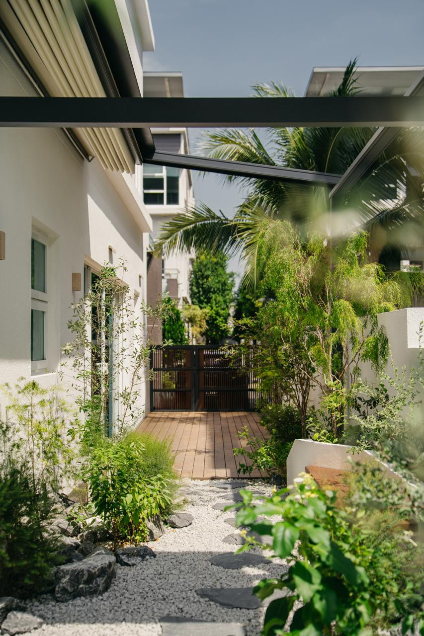 A timber deck and dark steel gate anchor the entry, framed by gravel, volcanic rock, and plantings that soften the boundary between street and home