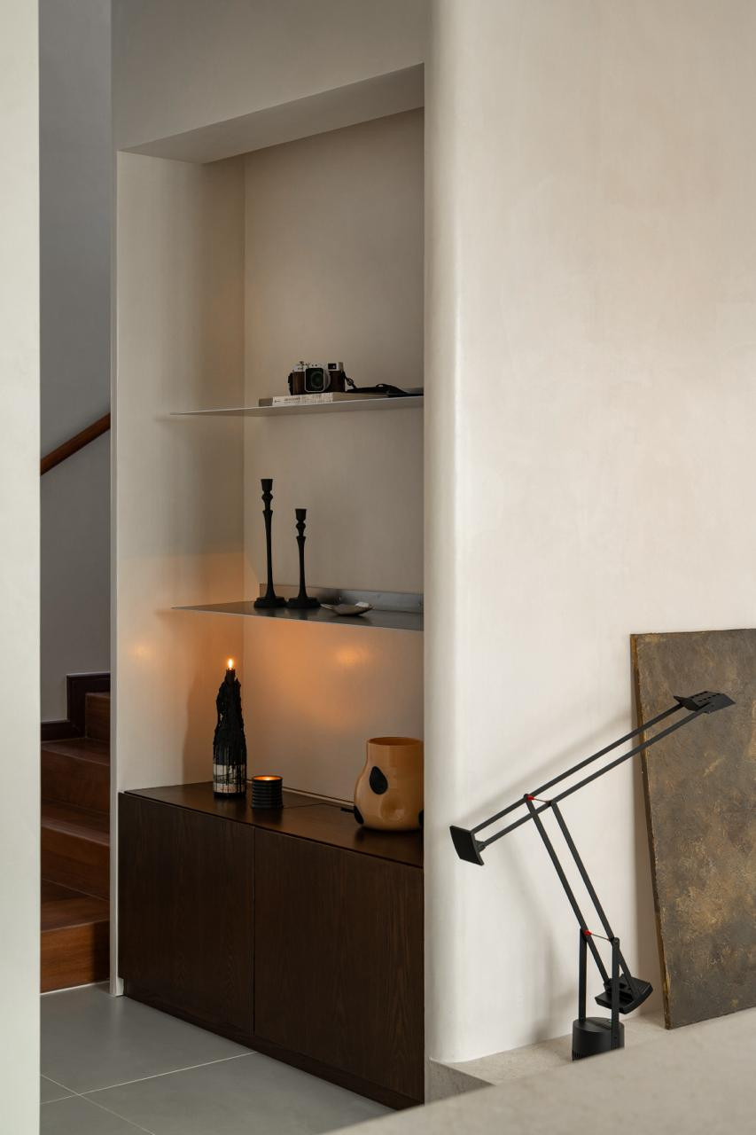 A recessed display niche houses candles and decorative objects above a dark oak sideboard; the Artemide Tizio lamp and an impasto artwork lean against the adjacent wall