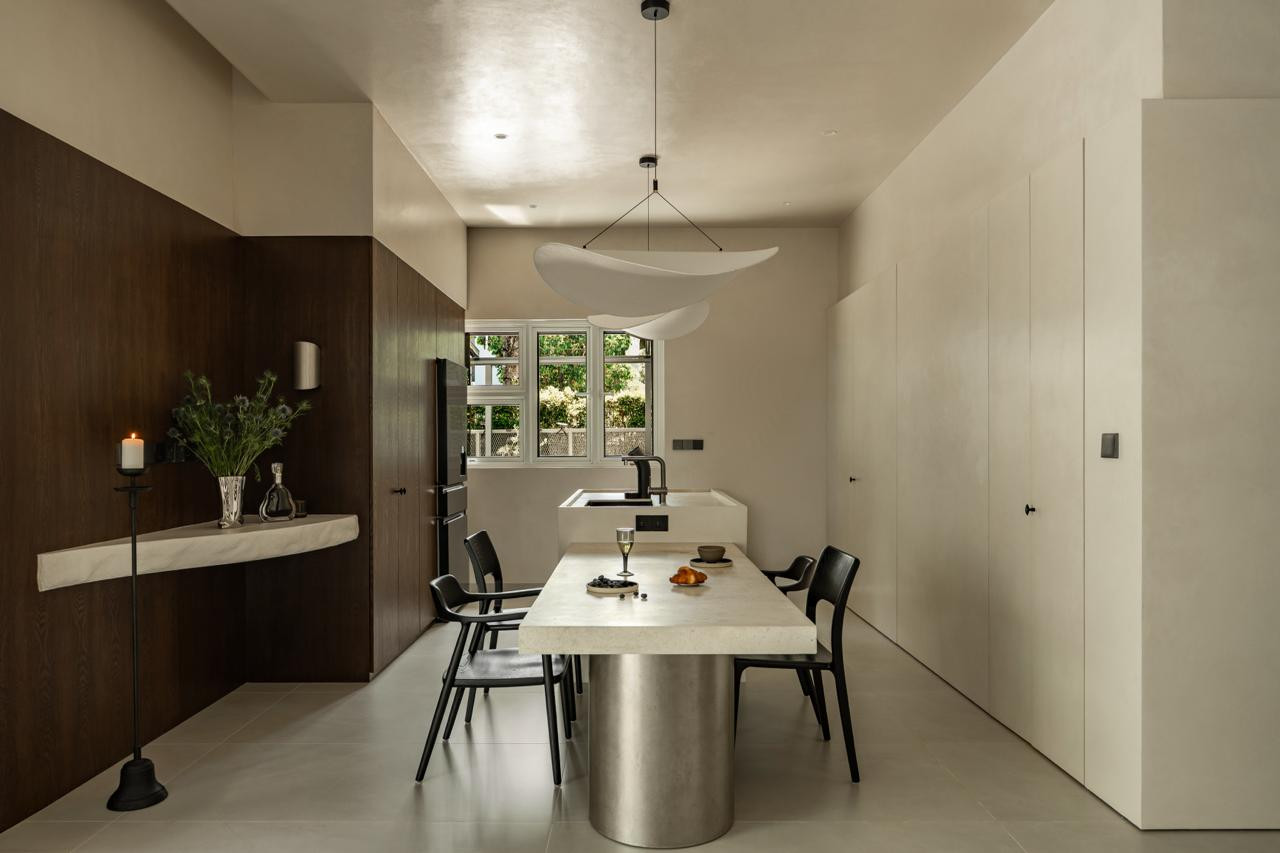 The dining room: a limestone table on a brushed steel base beneath a white biomorphic pendant, flanked by dark oak wall panels and a floating stone console shelf